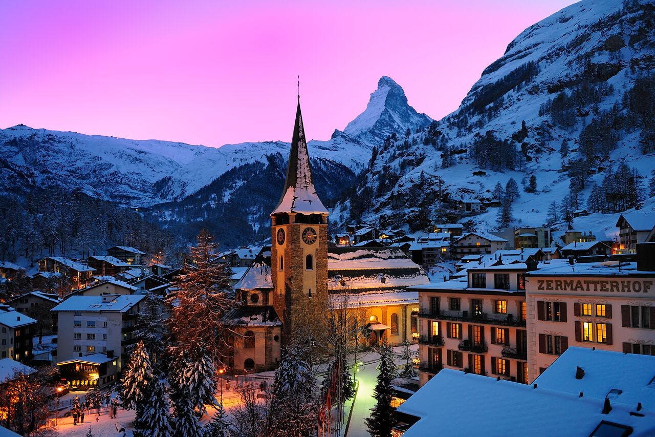 The snow-covered buildings of Zermatt with the Matterhorn mountain and a pink sunset sky