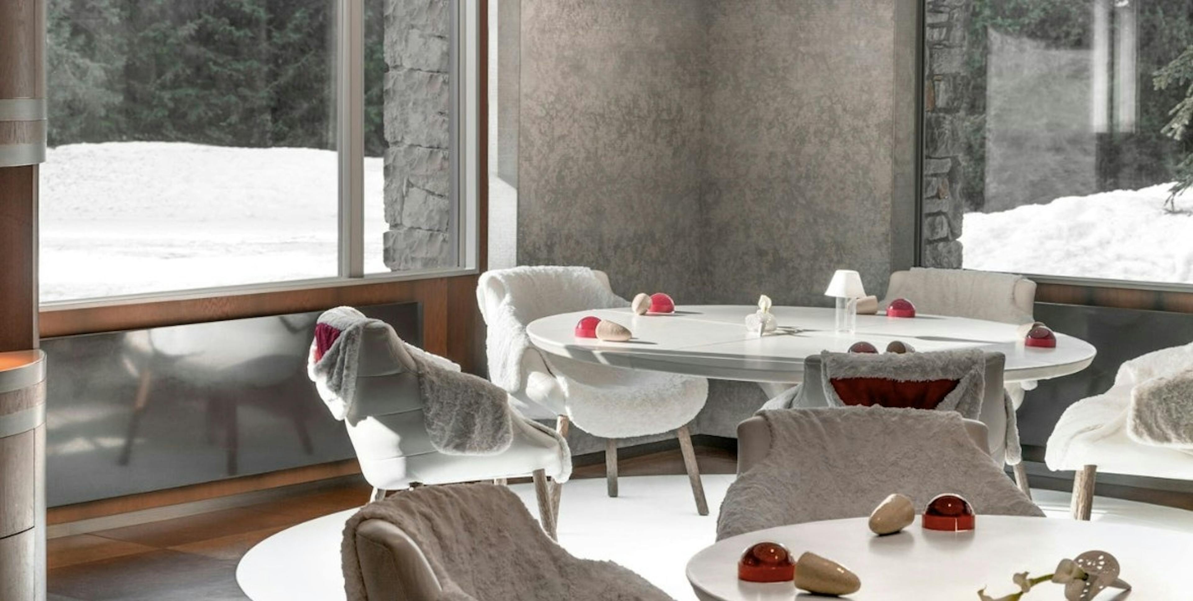 Modern white chairs surround white tables in the dining room of Le 1947 à Cheval Blanc