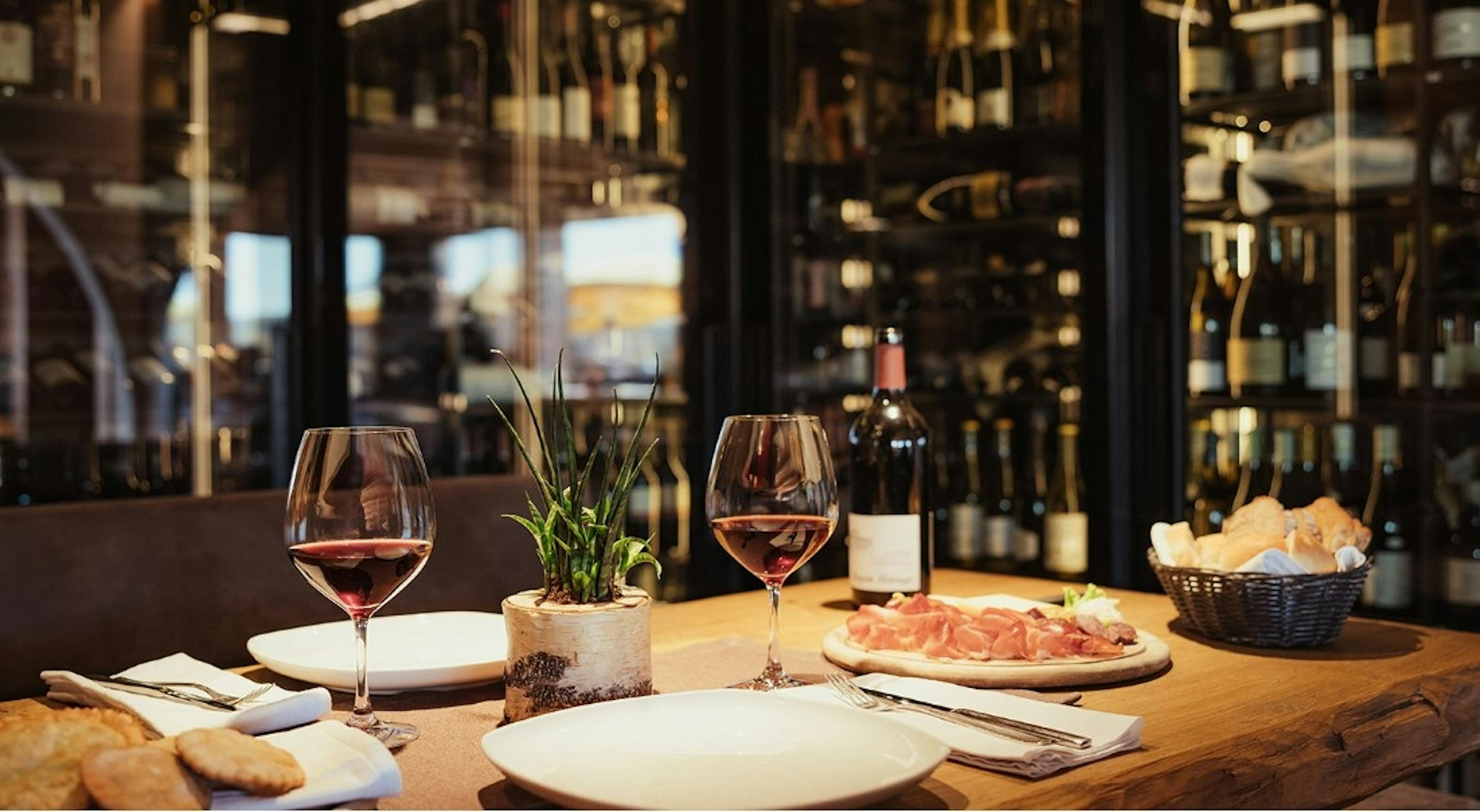 A wooden table set for two with red wine glasses, bread, and fresh meats at Rifugio Ütia de Bioch