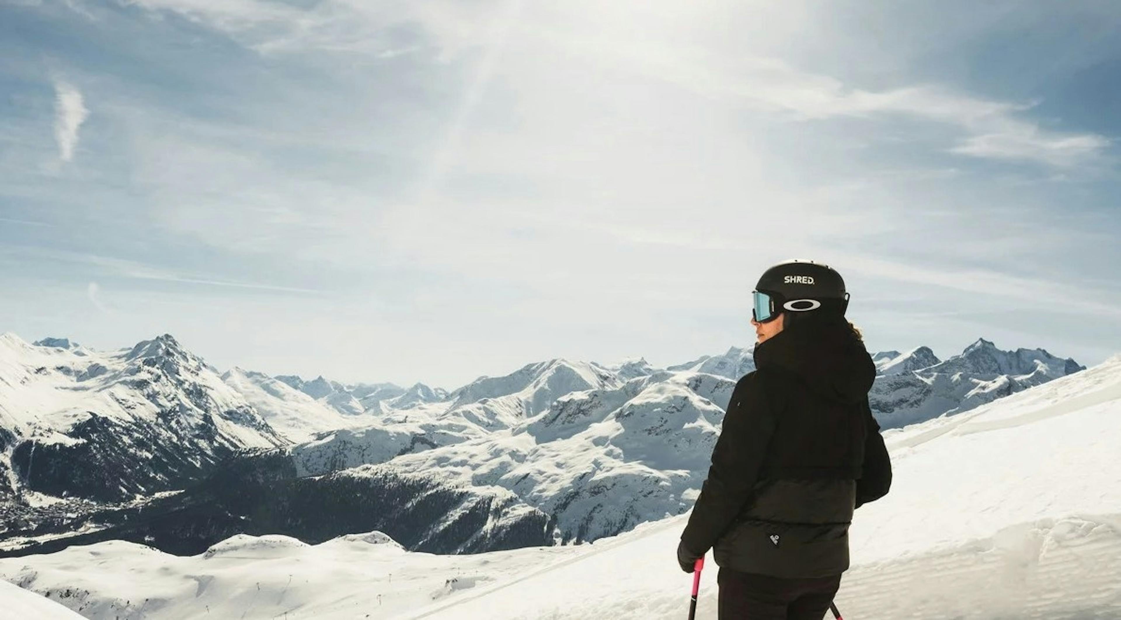 A skier looks at the view of snowy alpine mountains while standing at the top of a run on a sunny day at St. Moritz Resort