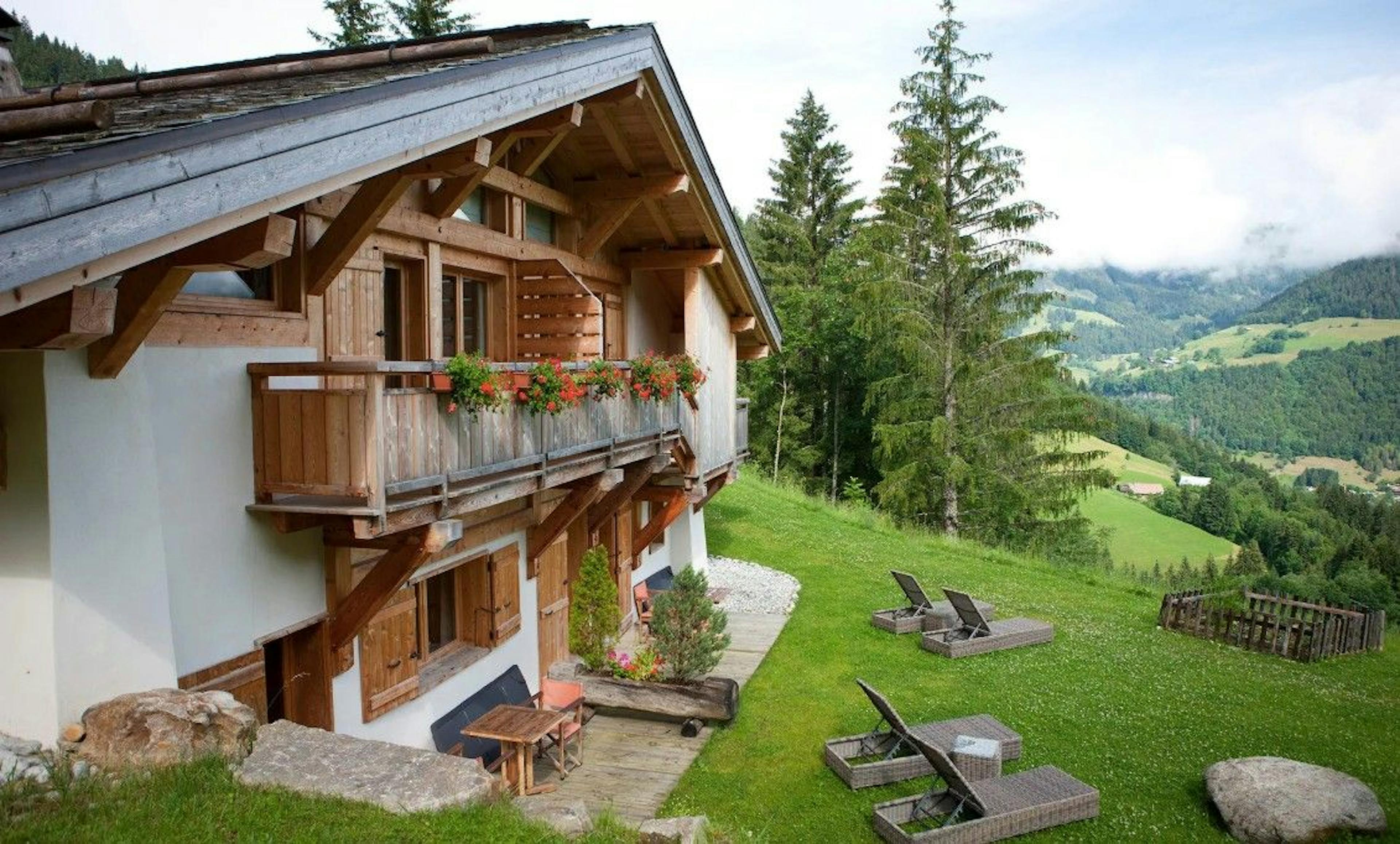 The rustic French hut of Flocons de Sel overlooks lush green alpine mountains filled with trees and grass