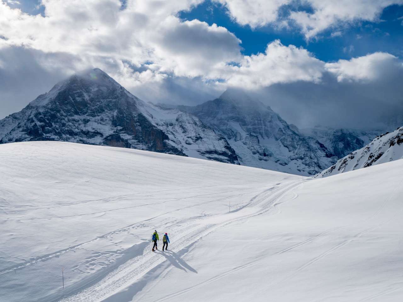 Aerial shot of two skiers of undiscernible gender hiking the misty slopes at Wengen, Switzerland.