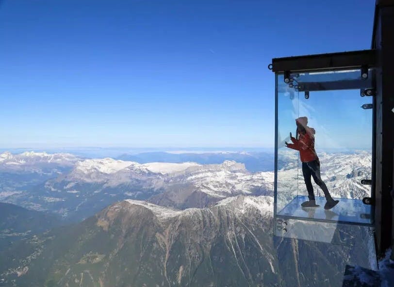 A woman stands in the glass box called Le Pas dans le Vide at the top of Aiguille du Midi Cable Car in Chamonix, France