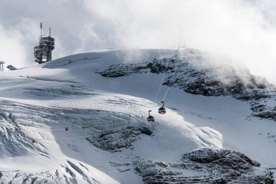 Two Titlis Rotair cable cars soar over the snowy Swiss Alps on a partly cloudy day