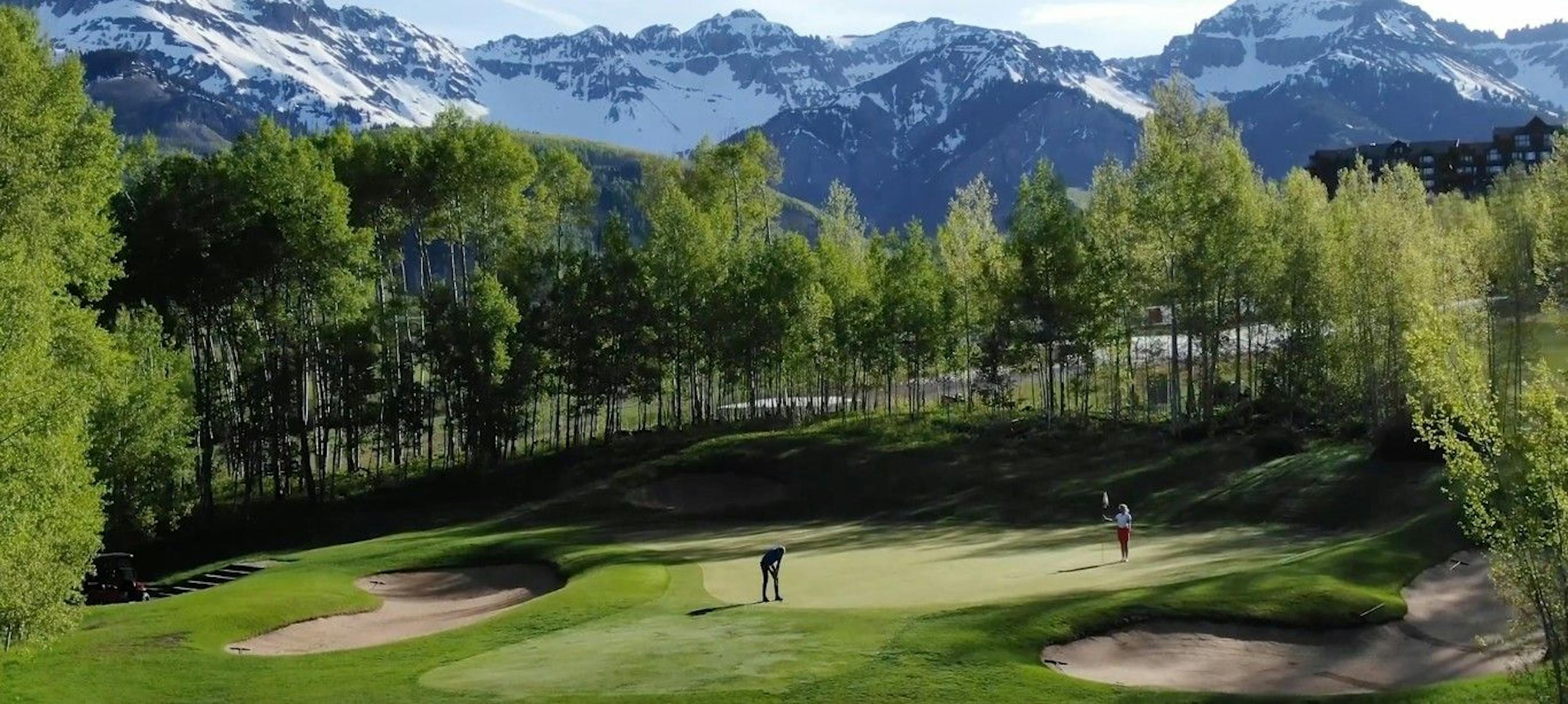 Two golfers standing on the golf course at Telluride Ski and Golf Club surrounded by trees and snowy mountains