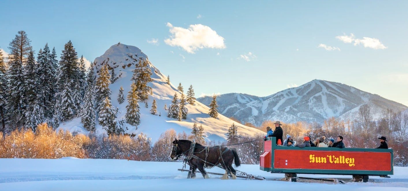 A group of people enjoy a horse drawn snowy sleigh ride with Sun Valley Ski Resort in the background
