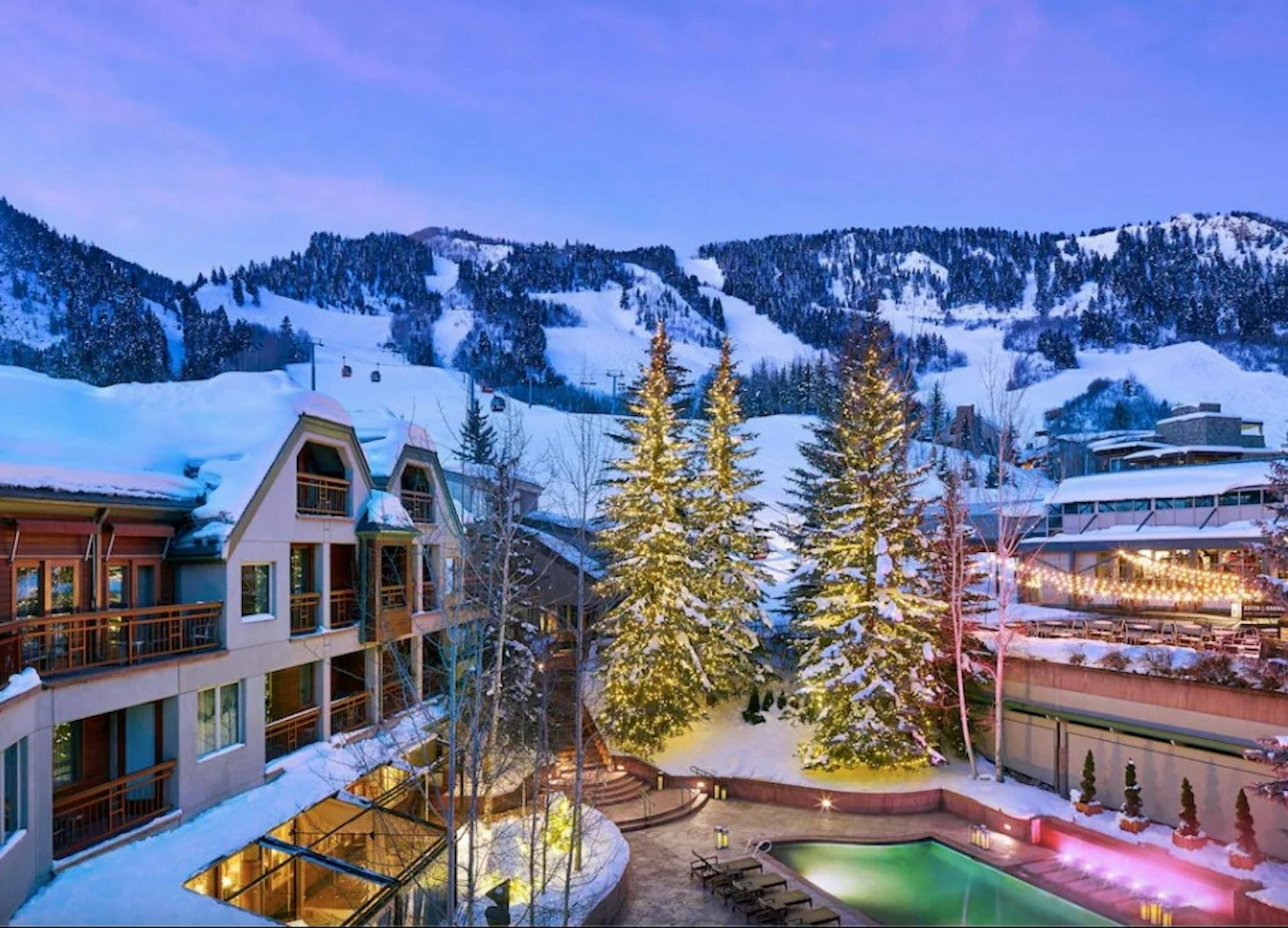 The Little Nell building and outdoor pool with snowy Aspen Snowmass Ski Resort in the backdrop
