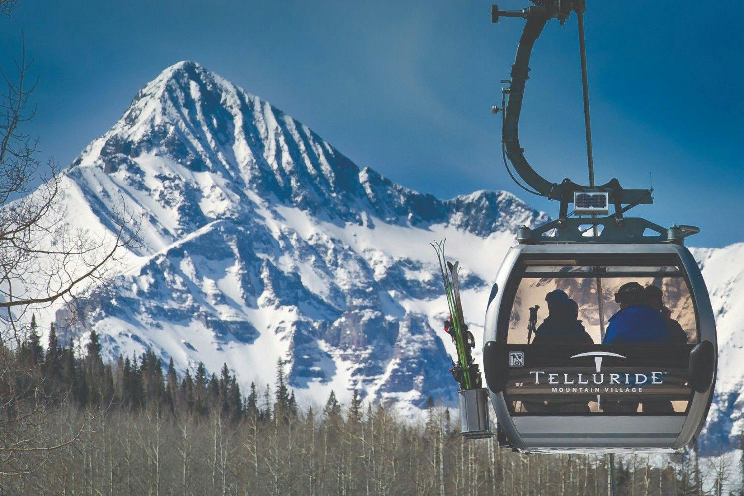 Two skiers sit in the Telluride gondola overlooking a snowy alpine mountain