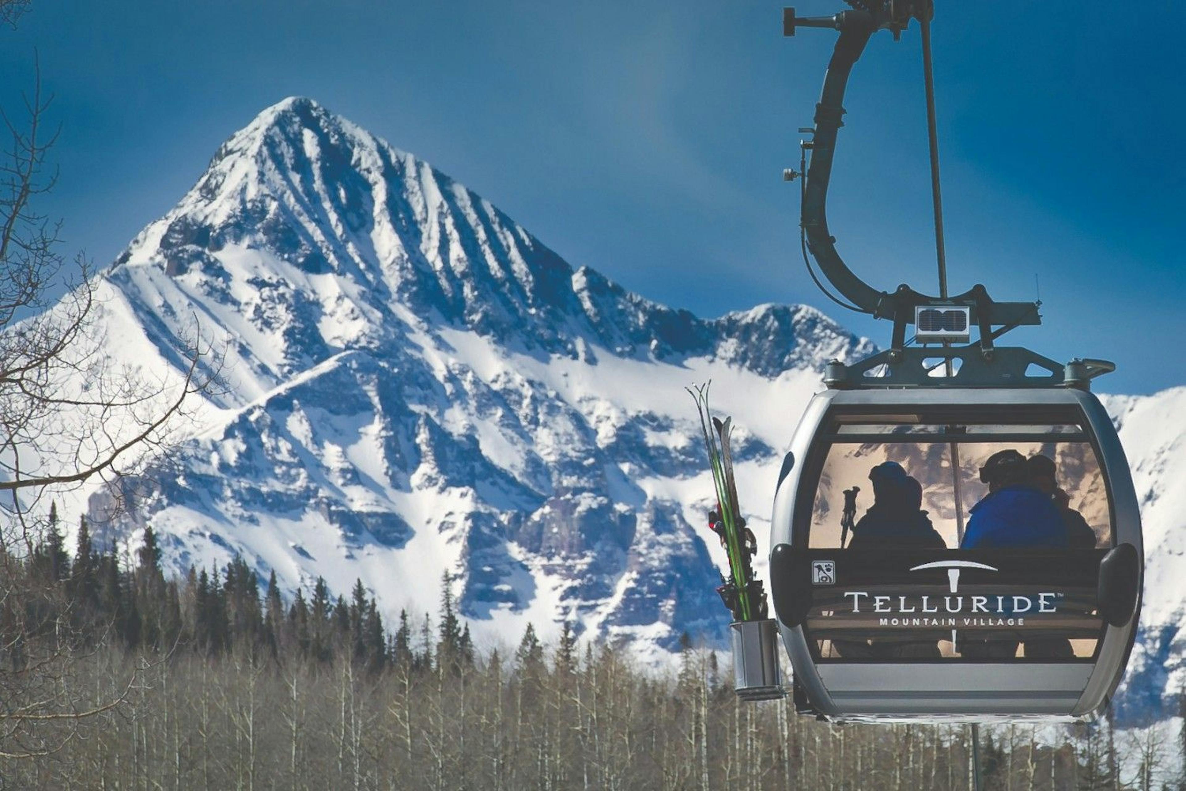 Two skiers sit in the Telluride gondola overlooking a snowy alpine mountain