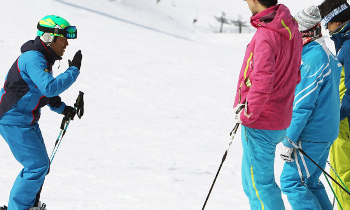 Male ski instructor giving a lesson to three diverse adult skiers in brightly-colored clothing at Nozawa Onsen in Japan.