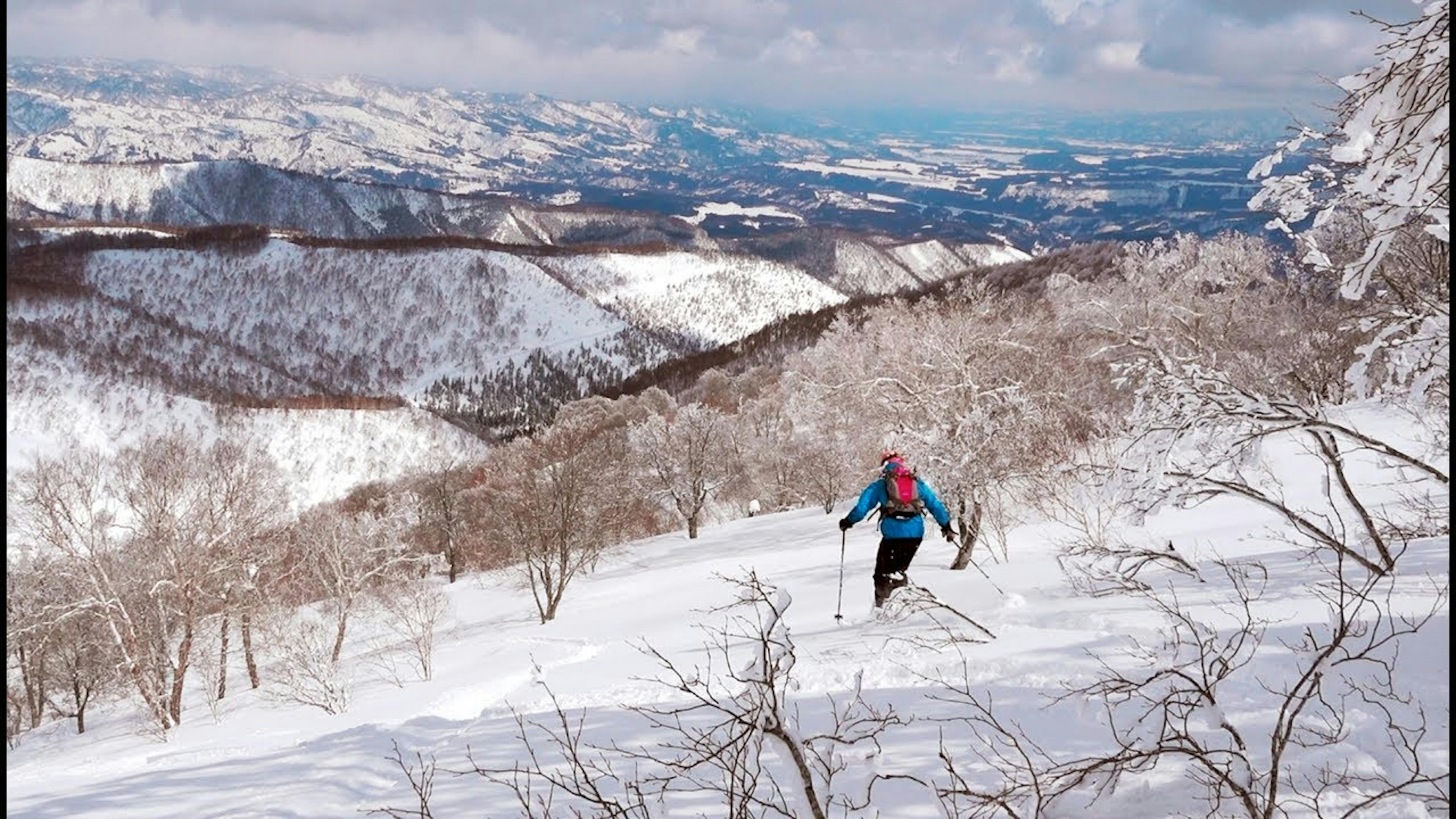 Skier of undiscernible gender in teal ski jacket and black ski pants hitting the backcountry off-piste slopes at Nozawa Onsen in Japan. 