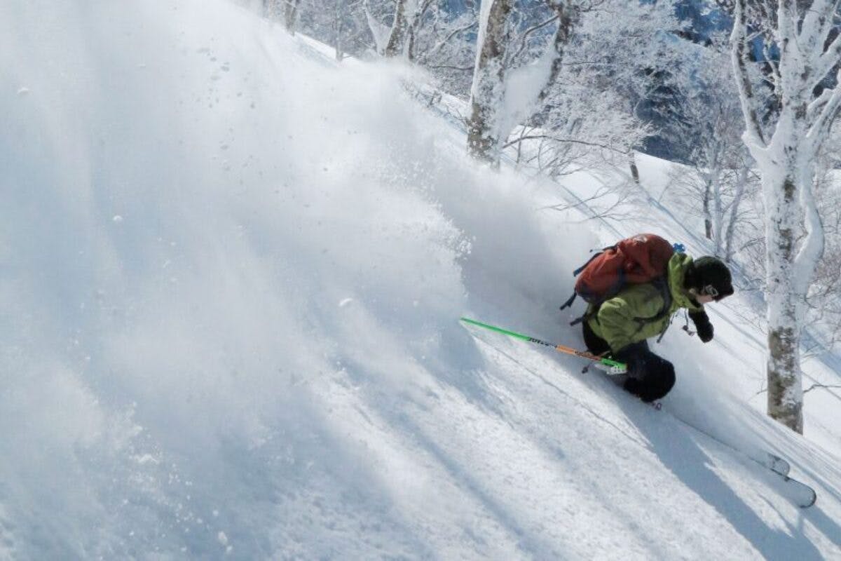 Skier of undiscernible gender in lime green ski jacket hitting the slopes at Nozawa Onsen in Japan.