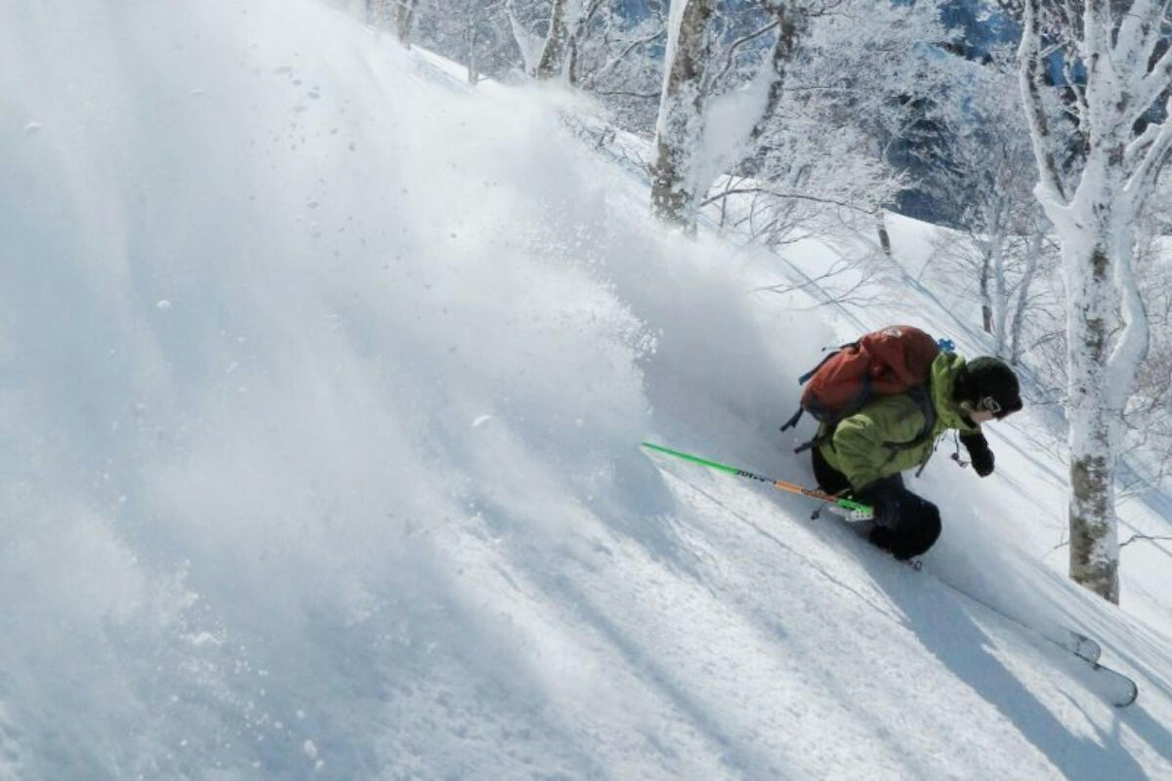 Skier of undiscernible gender in lime green ski jacket hitting the slopes at Nozawa Onsen in Japan. 