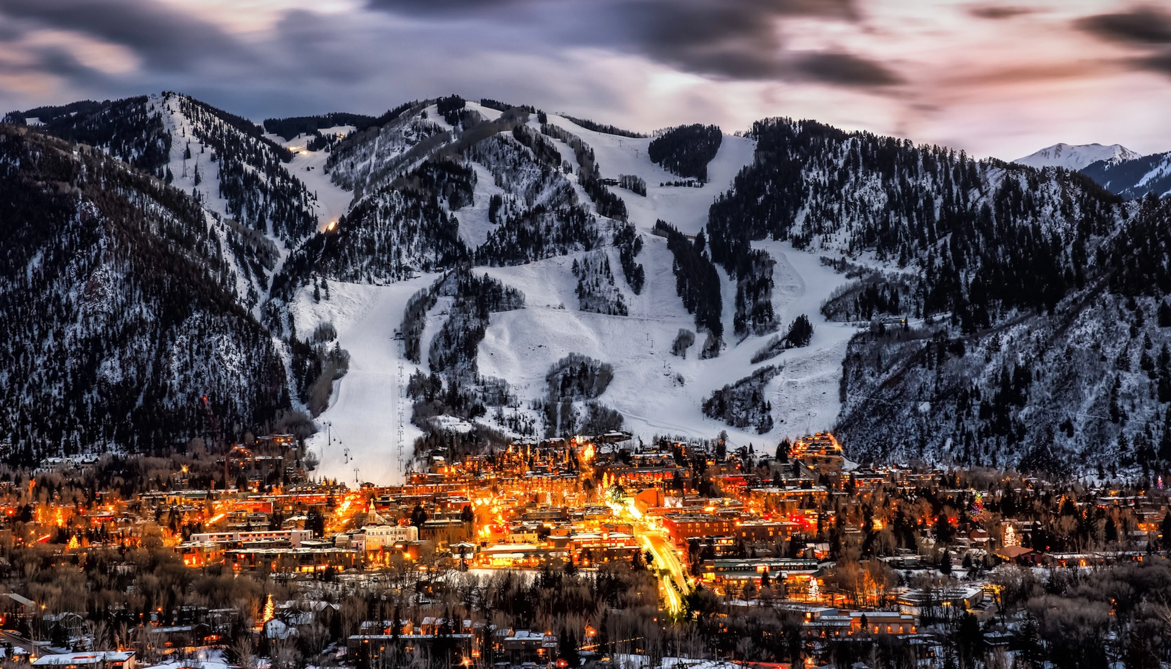 A mountain town glowing at dusk beneath snow-covered ski runs