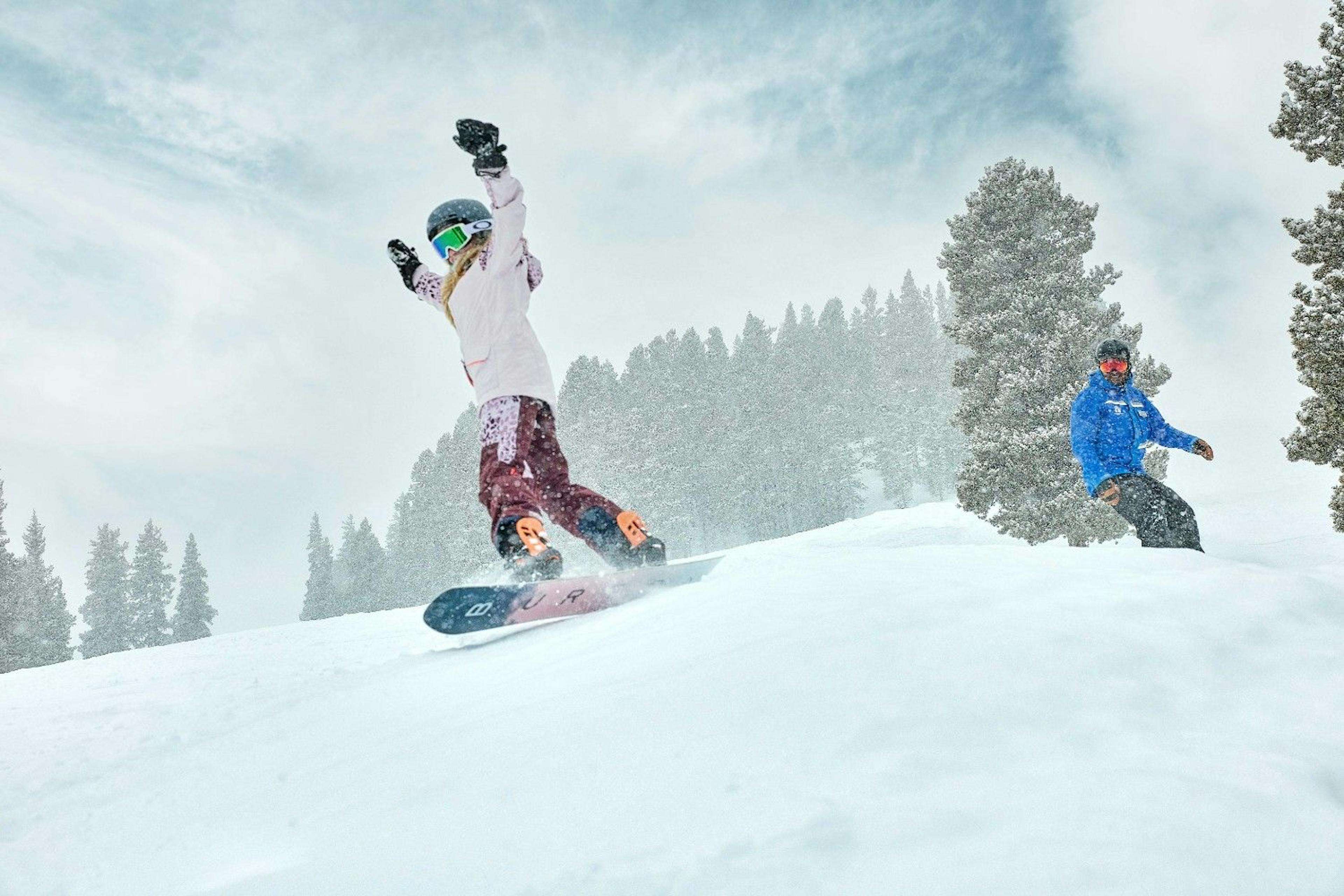 Child snowboarder cheers with arms up as they conquer a jump with a Breckenridge ski school instructor