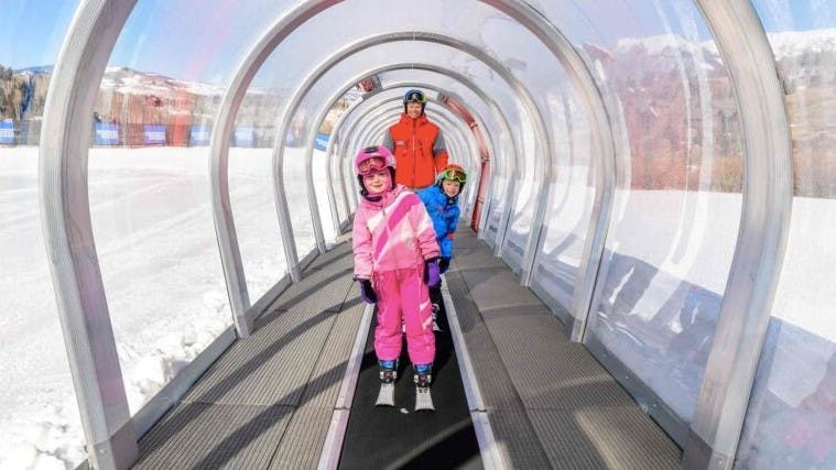 Two kids on skis ride the magic carpet ski lift with a Telluride ski school instructor