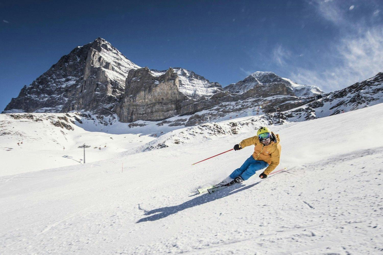 Skier in yellow ski jacket and blue ski pants hitting the slopes near Interlaken in the Jungfrau region of Switzerland.
