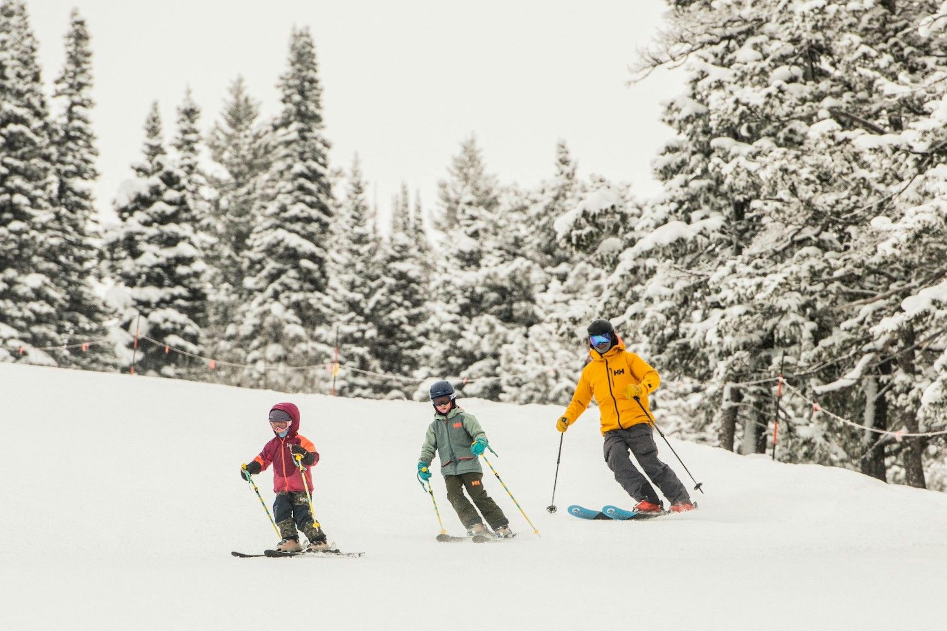 A parent and two kids skiing on a snowy day at Grand Targhee Resort