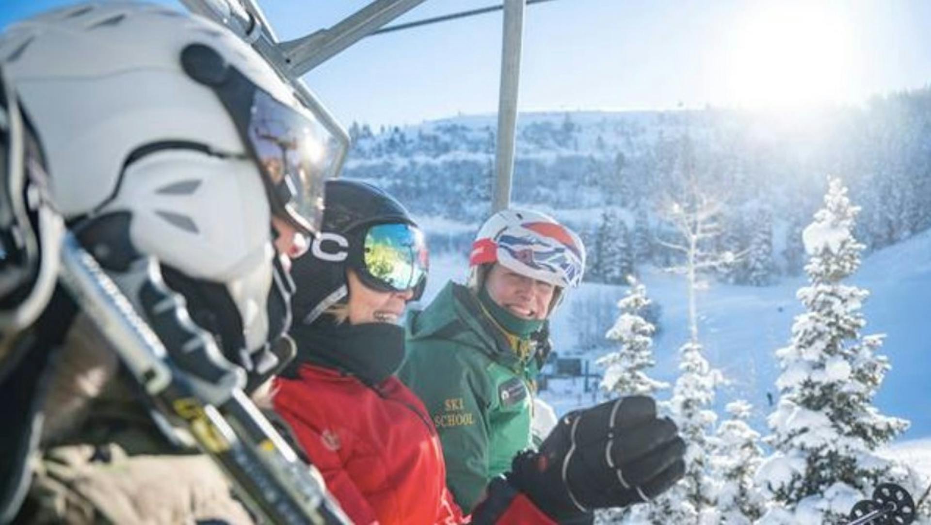 Deer Valley Resort Ski School instructor sitting and smiling on a chair lift with two other skiers on a beautiful sunny day