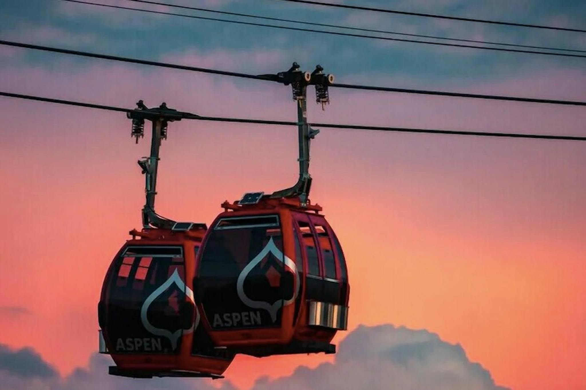 Two Aspen gondolas move along behind a pretty red and purple sunset sky