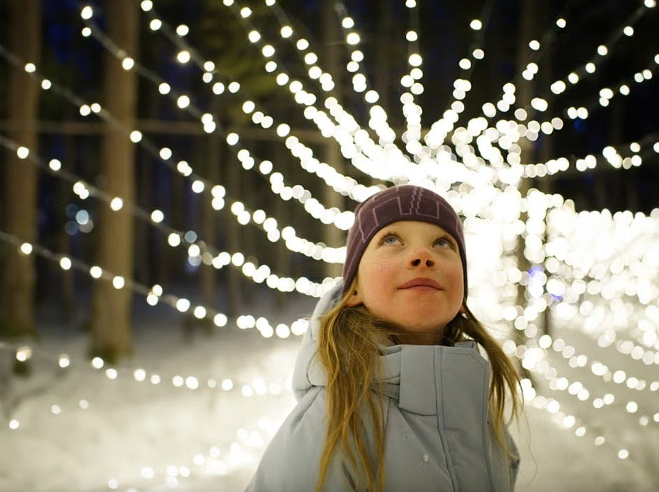 Little girl in a beanie and ski jacket looks up at a tunnel of twinkling lights