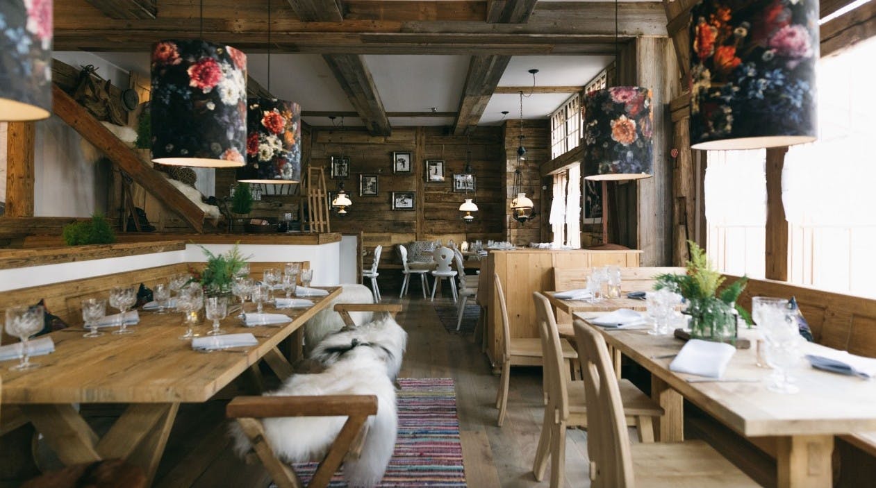 Wooden tables are set with plates and glasses, surrounded by wooden chairs and wooden walls in the Alpenrose restaurant