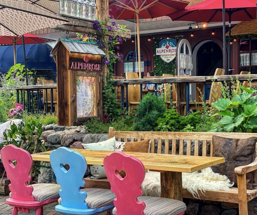 The outside patio with plants, umbrellas, a cozy wooden table and colorful chairs at Alpenrose restaurant