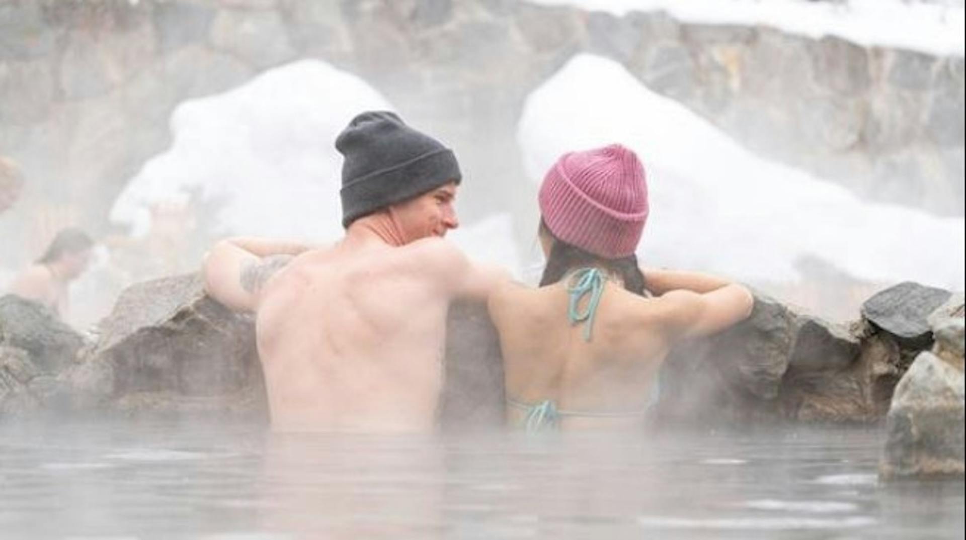 A man and woman wearing beanies and bathing suits while they soak in the Steamboat Springs hot springs