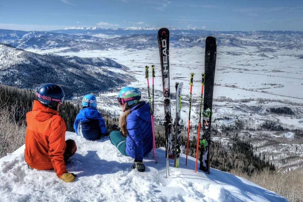 Parents with their child in ski gear taking a break to enjoy the snowy alpine view at the top of Streamboat Springs Resort