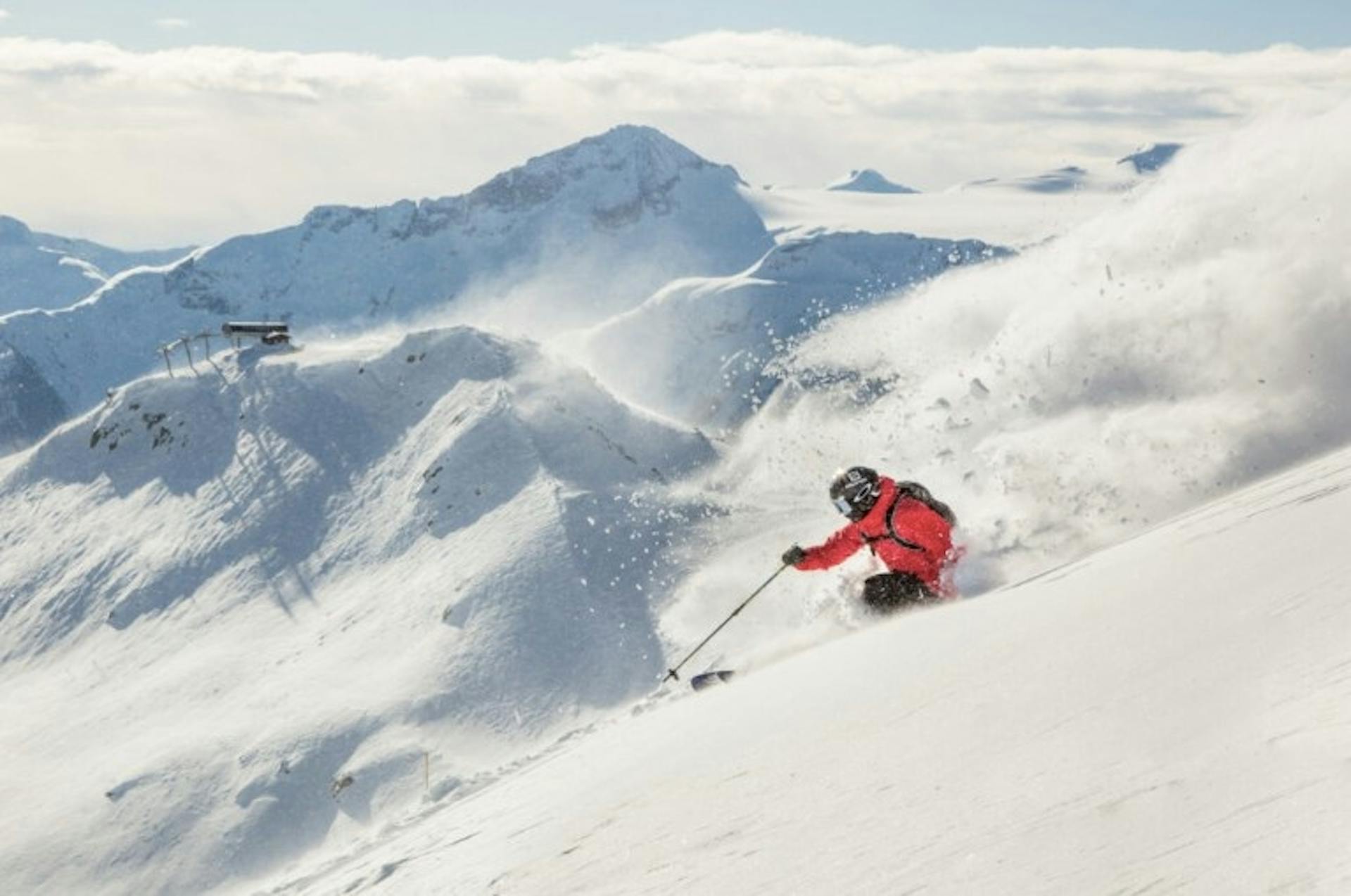 Skier skiing down a slope at Whistler Blackcomb spraying powder behind them with a snowy mountain backdrop