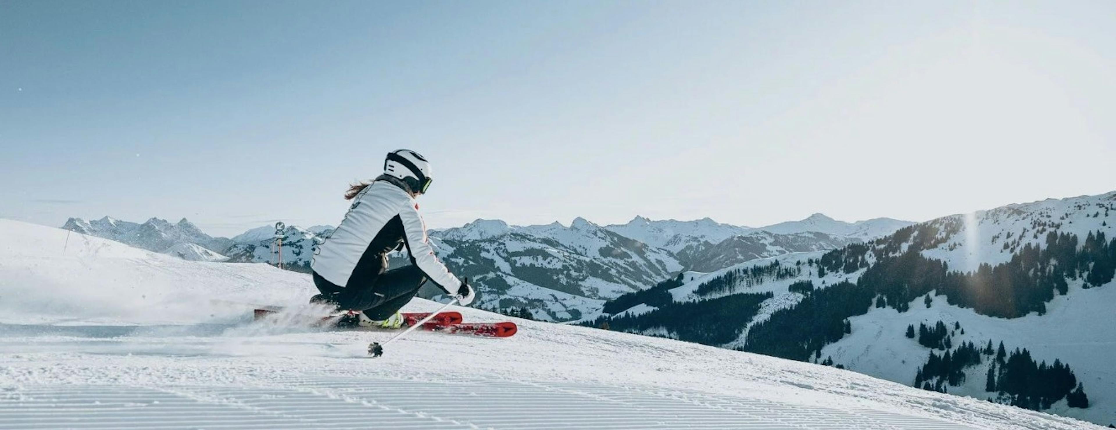 Skier turning on a freshly groomed run overlooking snowy mountains on a bluebird day at Kitzbühel Resort