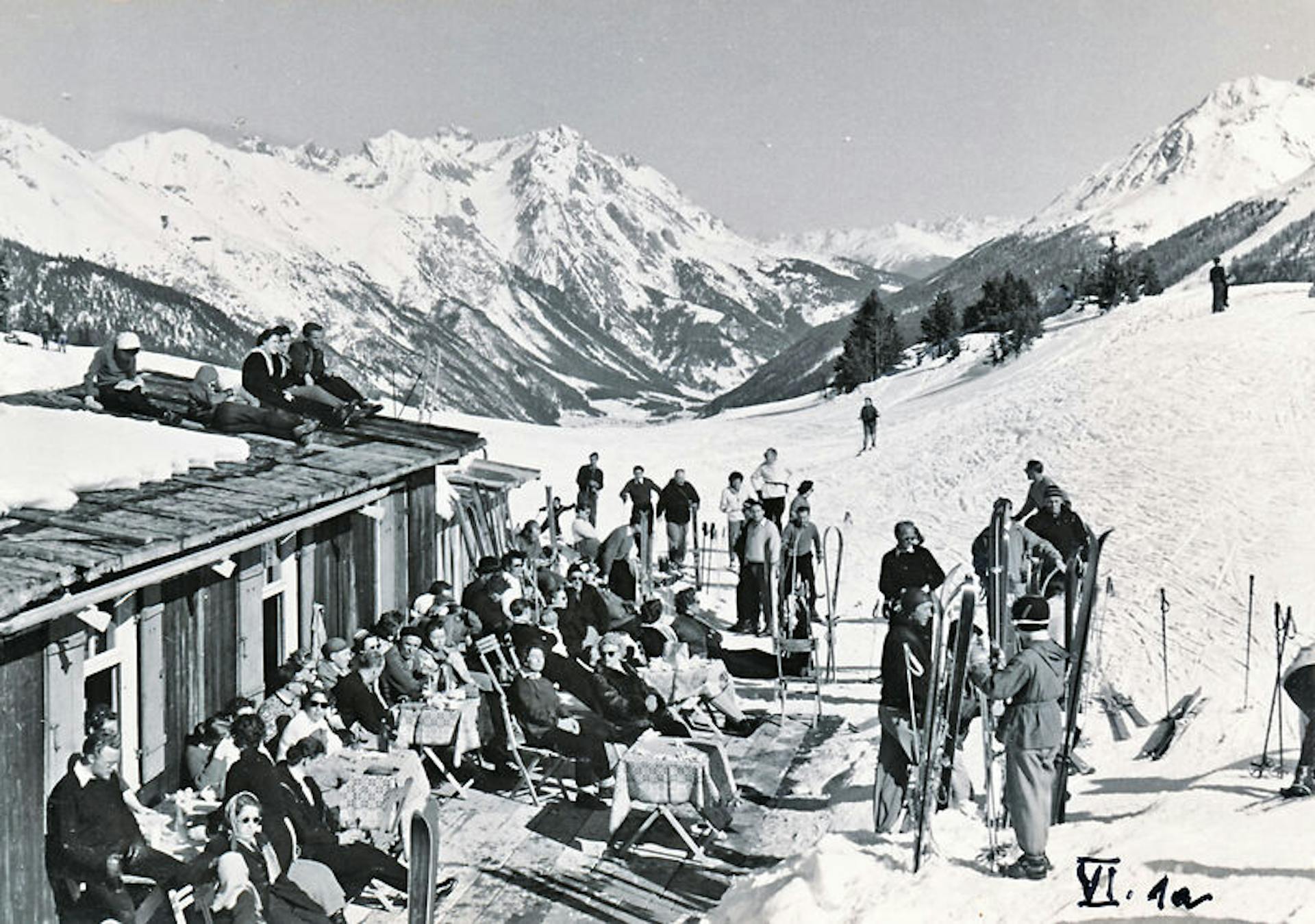 Black and white historic photo of a crowd of skiers hanging out next to a lodge at St. Anton am Arlberg