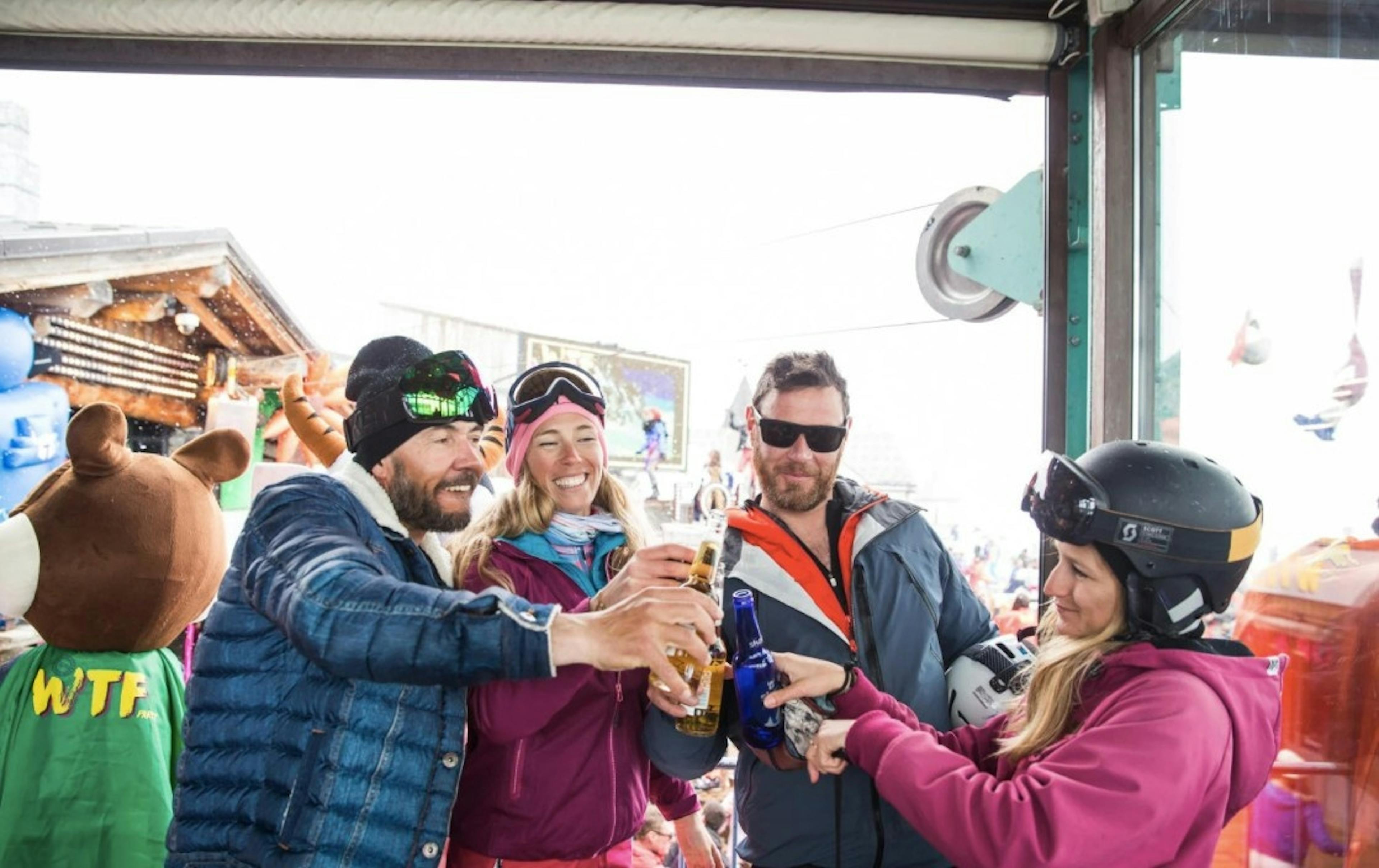 four smiling friends in ski gear cheers their drinks at an on-mountain bar at Val d’Isère Resort