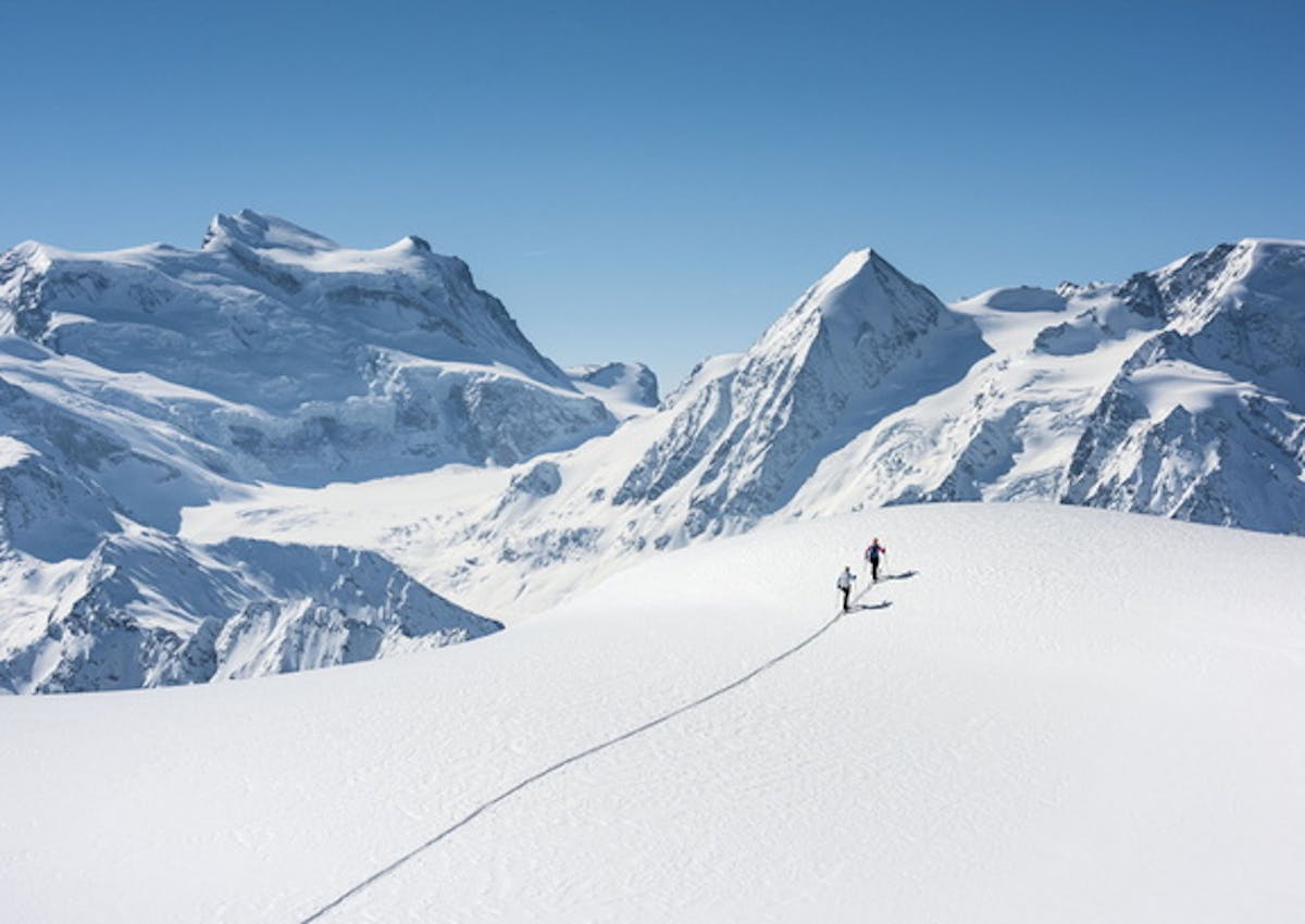 two backcountry skiers trekking through fresh snow up towards alpine mountains at Verbier Resort