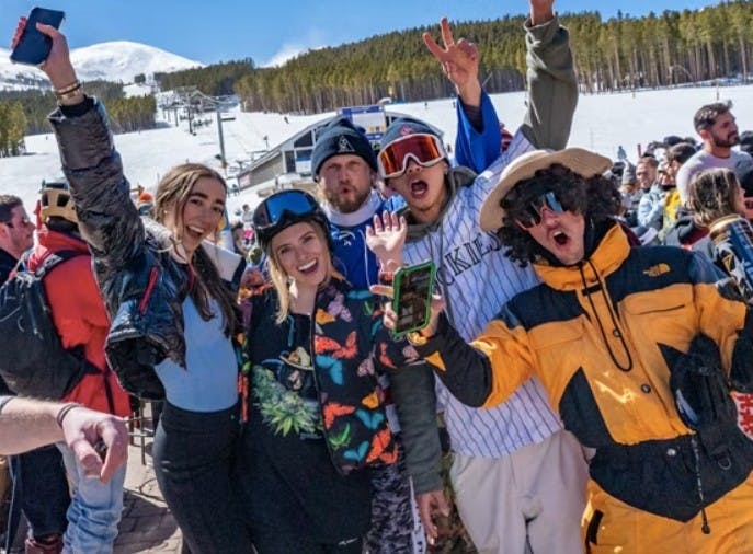 Group of five friends in winter gear smile and yell for the camera celebrating spring break in front of the slopes at Breckenridge Resort