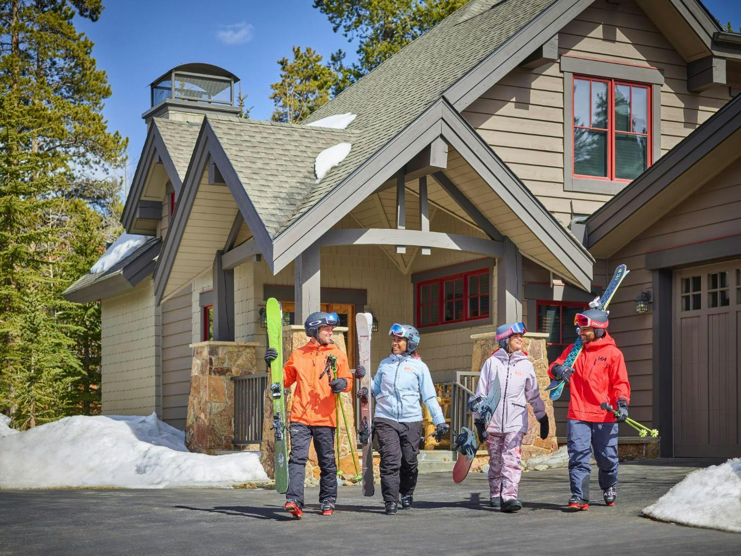 Group of four friends wearing winter sports gear and carrying skis and snowboards walking away from Mountain Thunder Lodge in Breckenridge