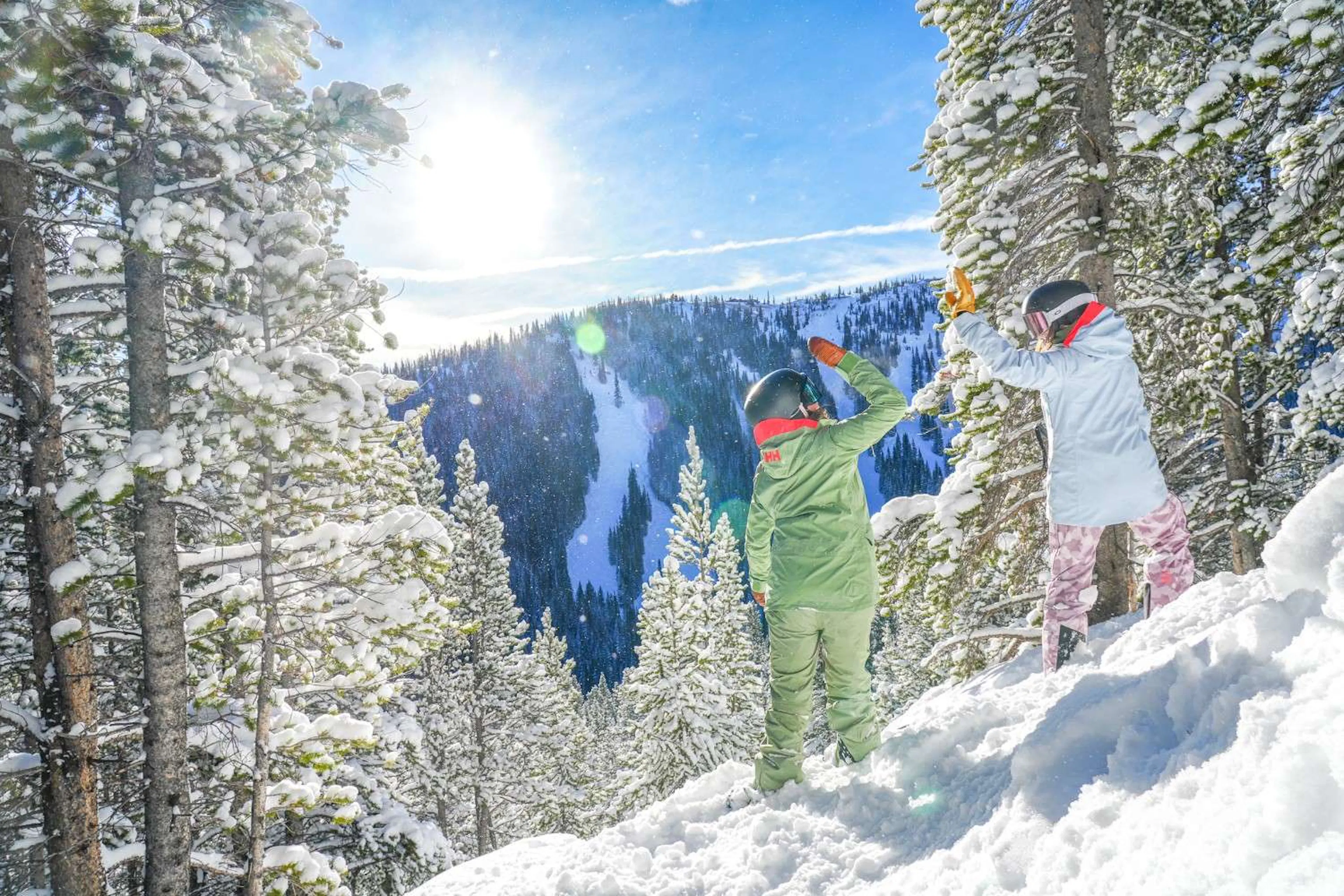 Two snowboarders high-five in powder on the sunny slopes overlooking Breckenridge Resort