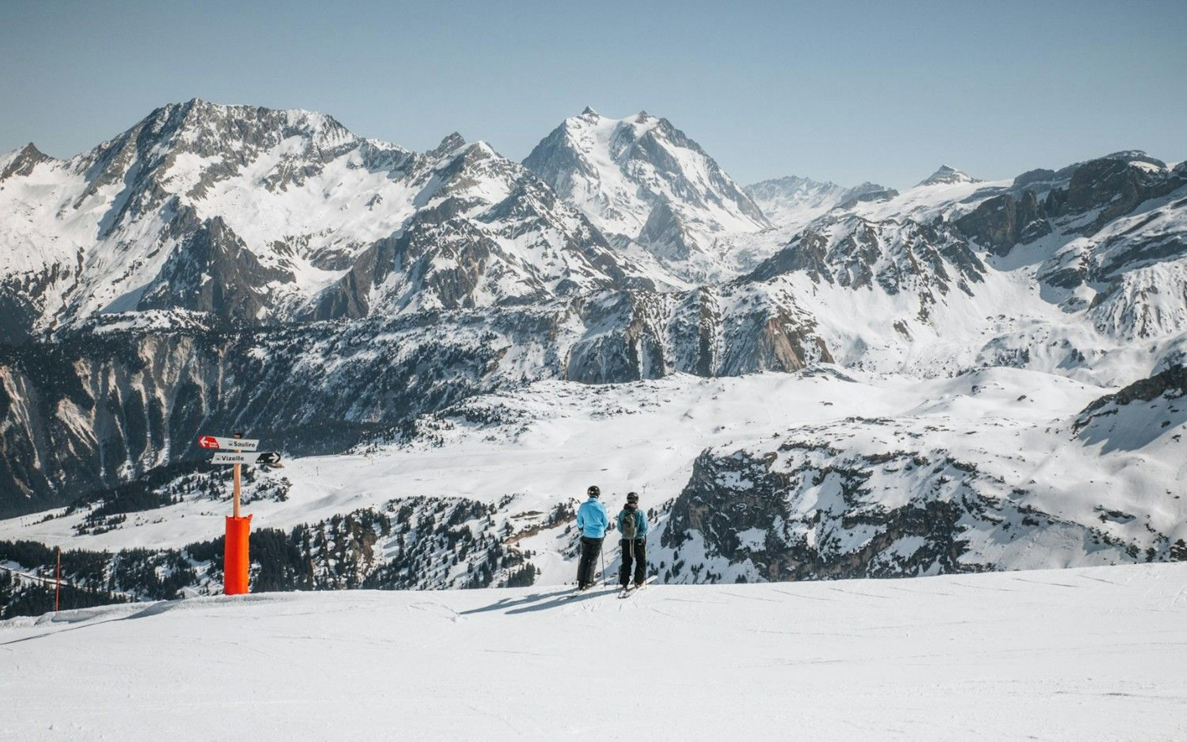 two skiers stand at the top of the slopes at Courchevel overlooking the snowy French Alps