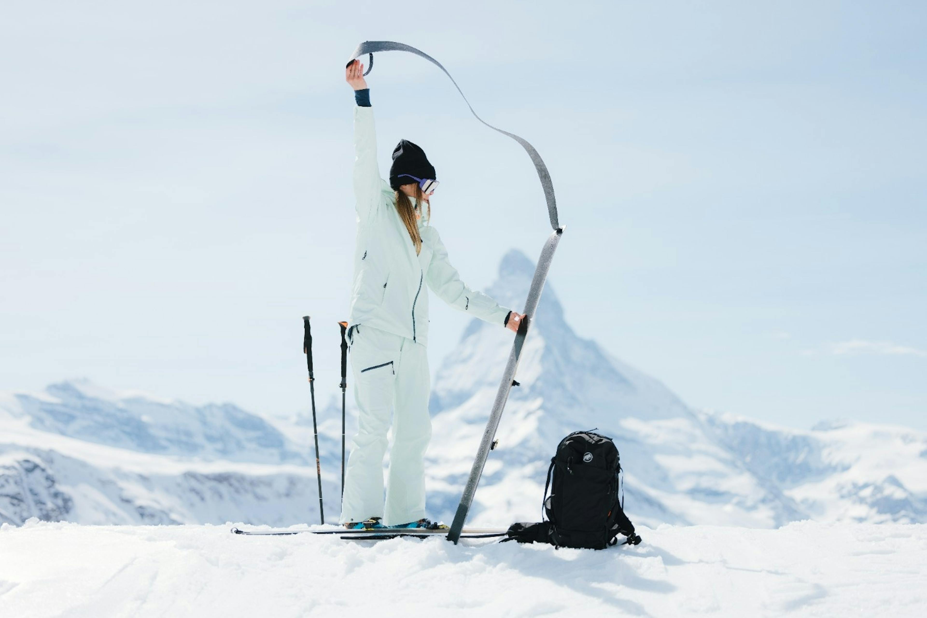 woman skier takes off the skins on her skis with her backpack nearby gearing up for backcountry skiing