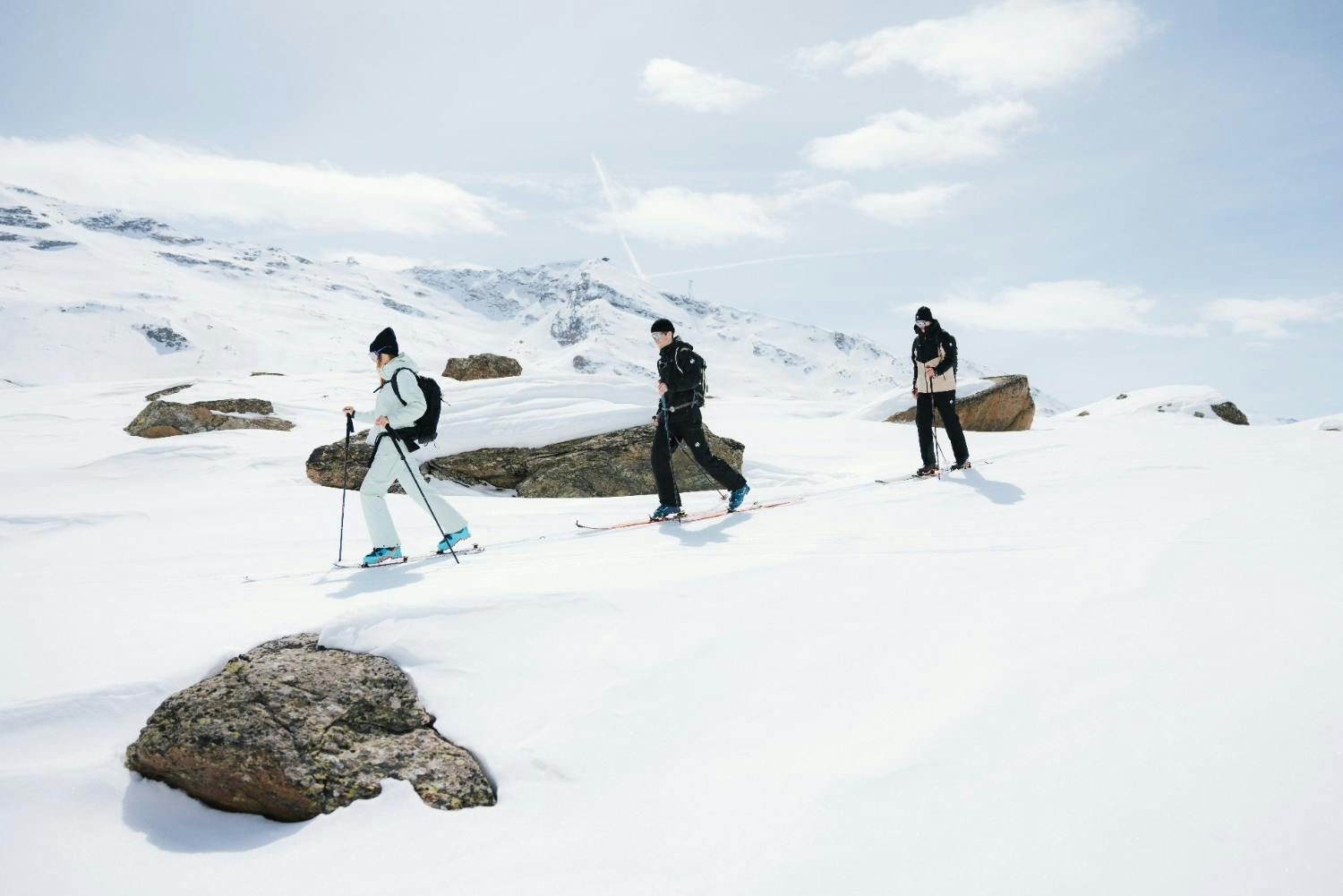 3 skiers in winter gear skinning uphill snowy backcountry terrain