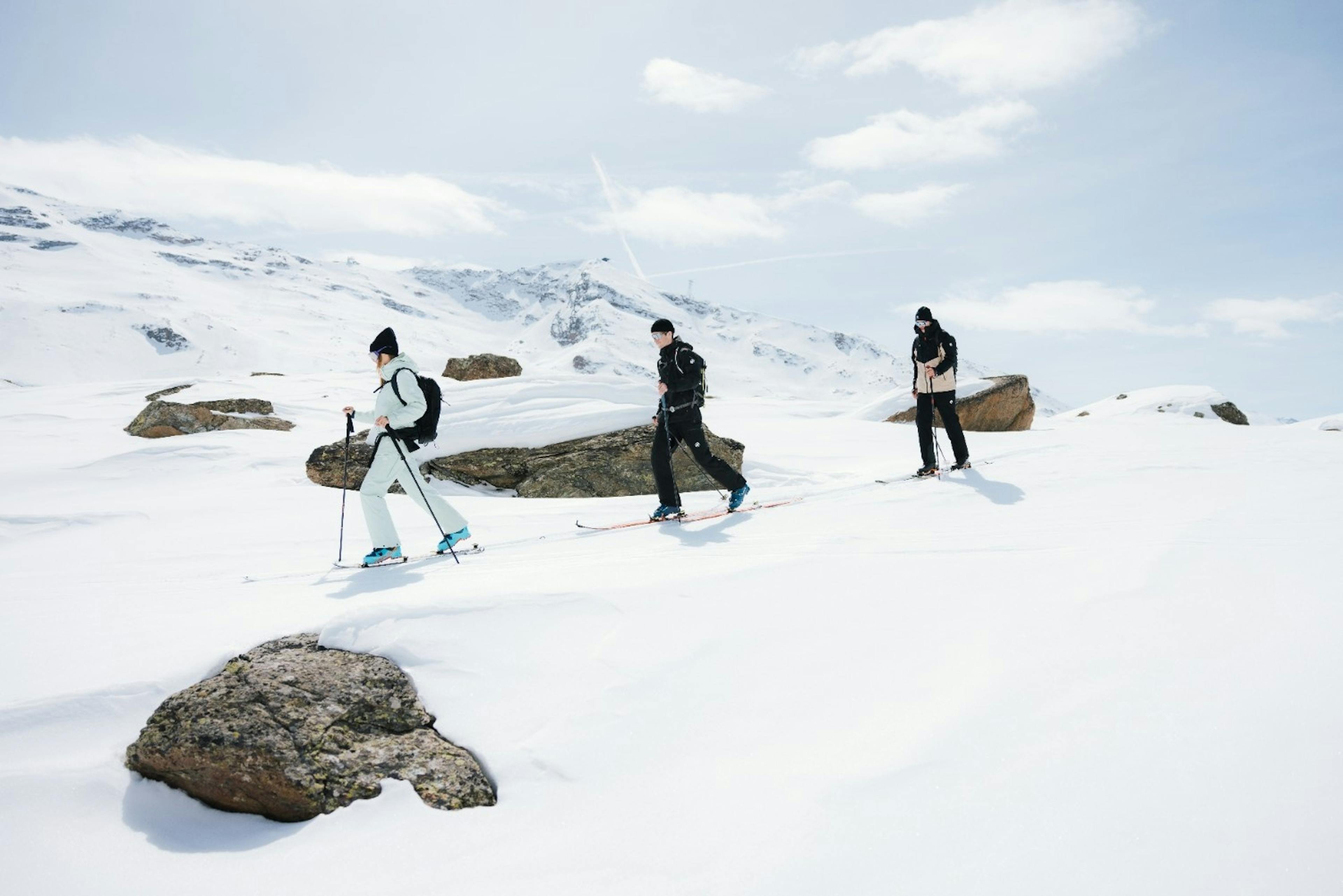 3 skiers in winter gear skinning uphill snowy backcountry terrain