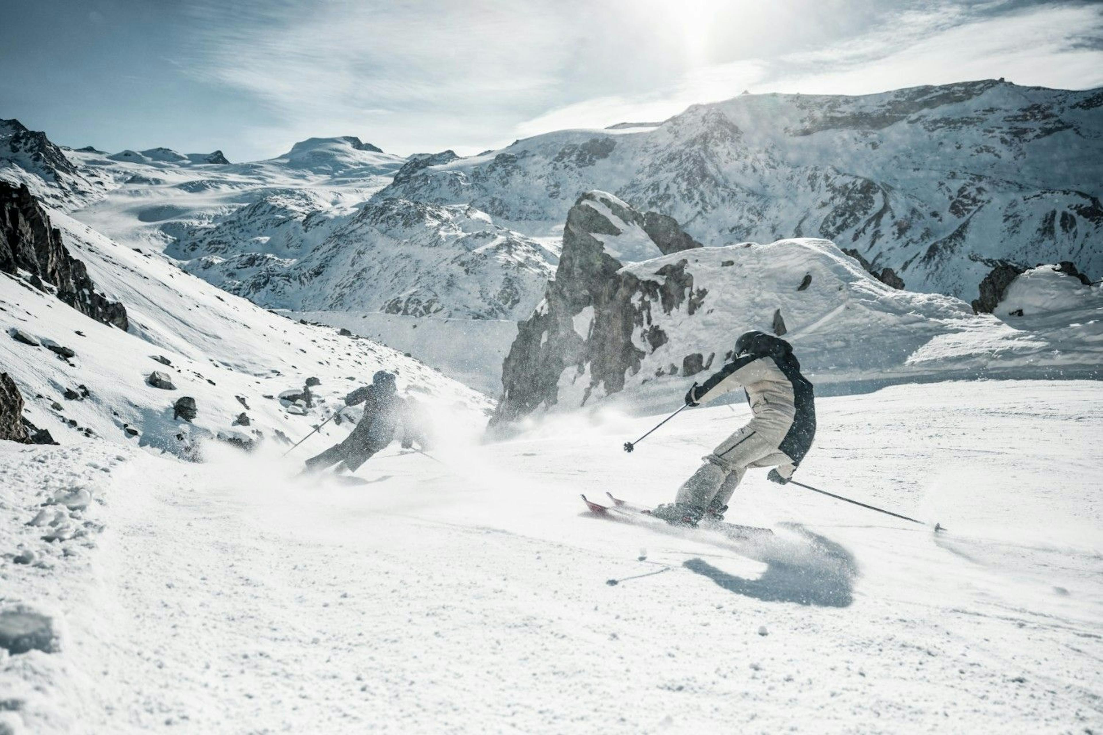 two skiers sending it down the snowy backcountry slopes on a bluebird day