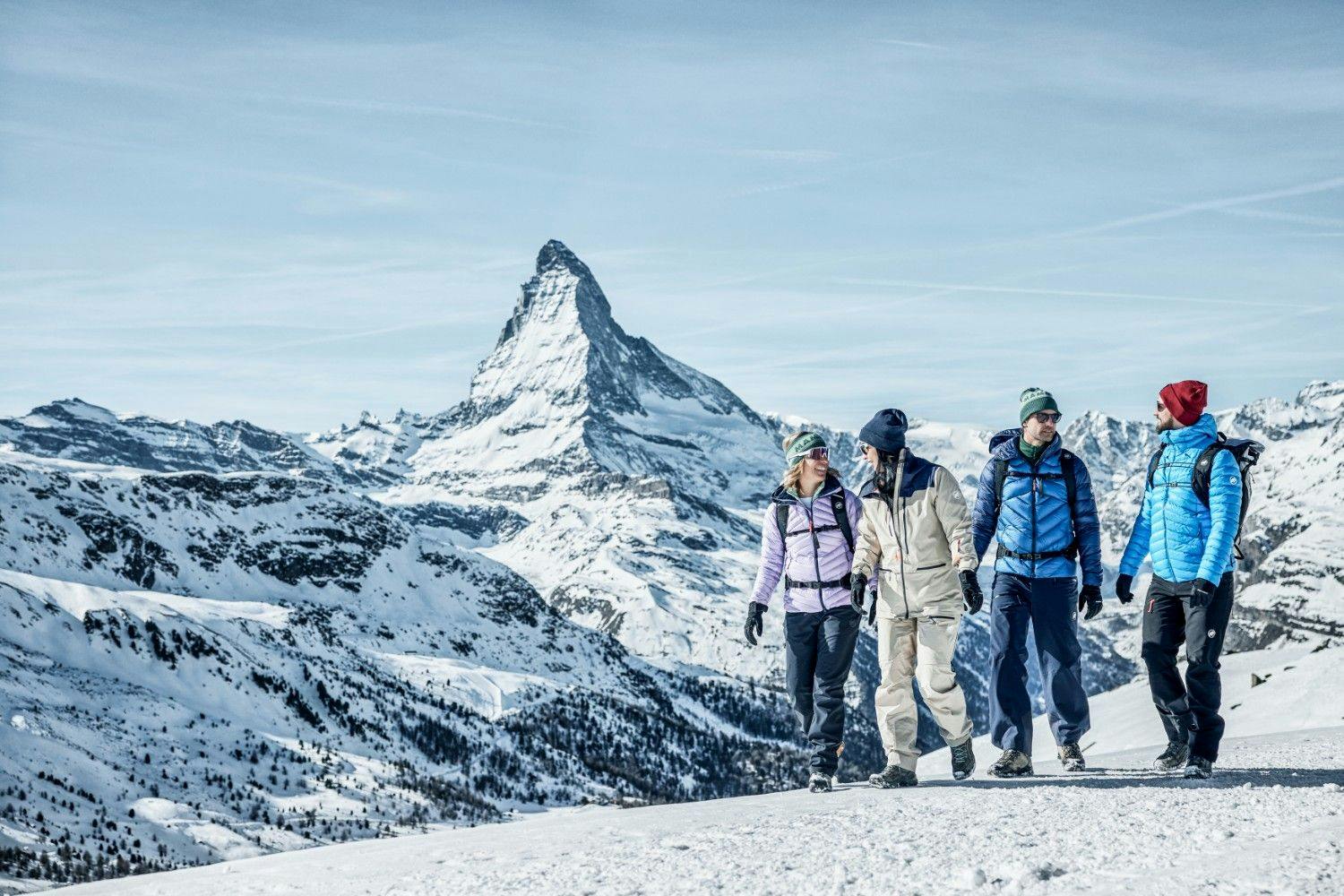 Four friends talking and walking in snow gear at Zermatt ski resort with the Matterhorn mountain behind them