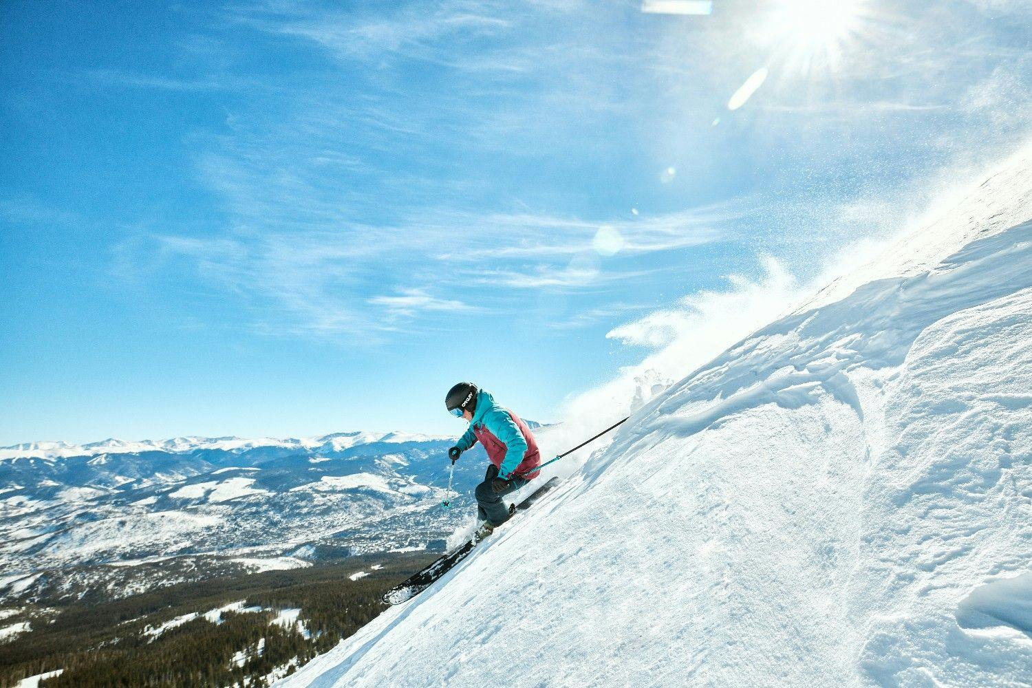 Skier shitting fresh powder on a steep slope at Breckenridge Resort on a bluebird day
