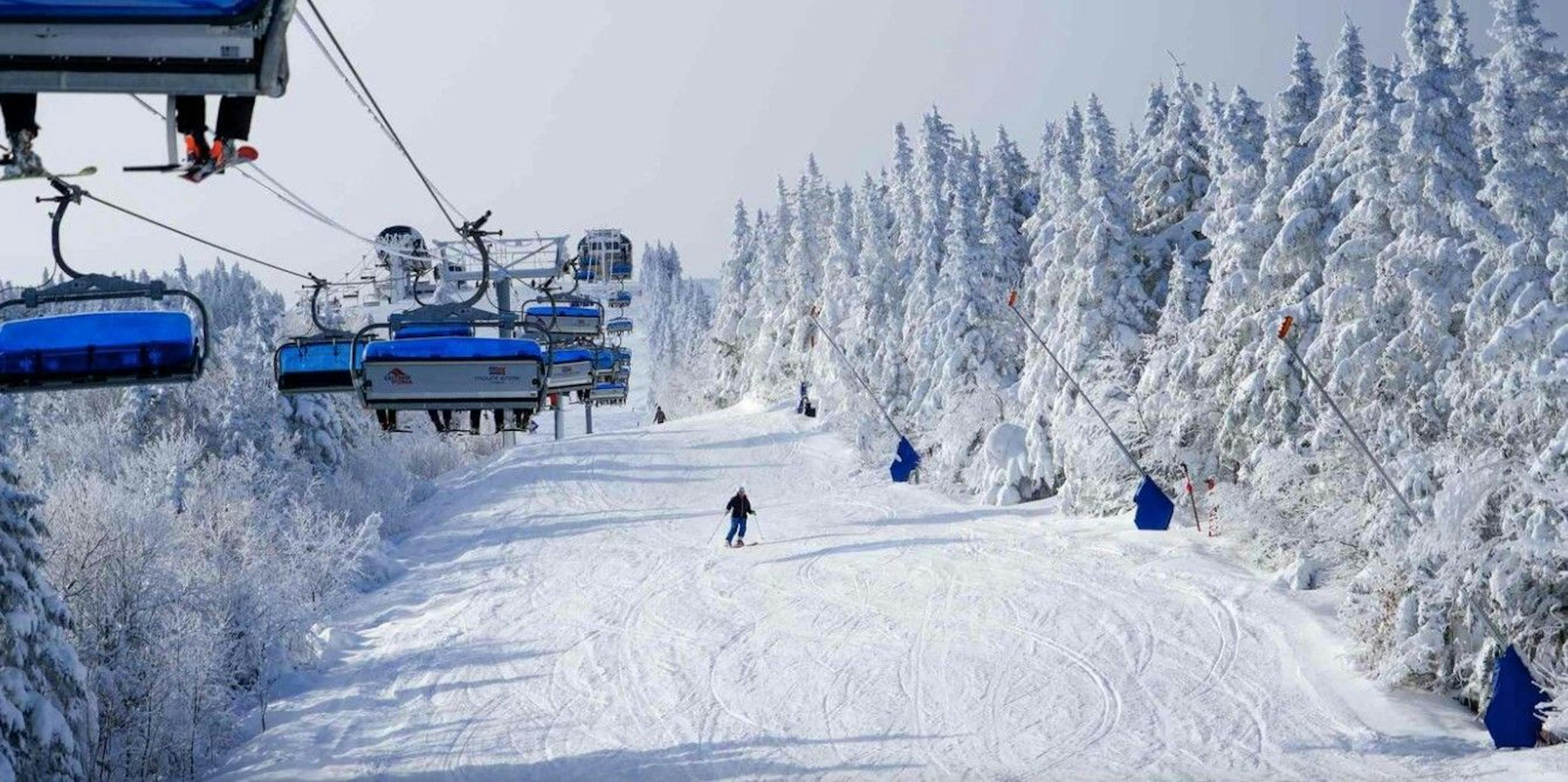A skier skiing down a run at Mount Snow Resort under the ski lift, surrounded by snow-covered trees