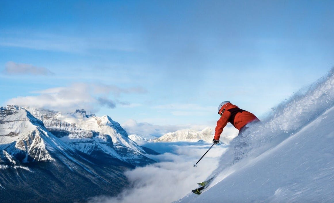Skier skiing down a steep slope spraying powder on a bluebird day overlooking the mountains at Banff Lake Louise Resort