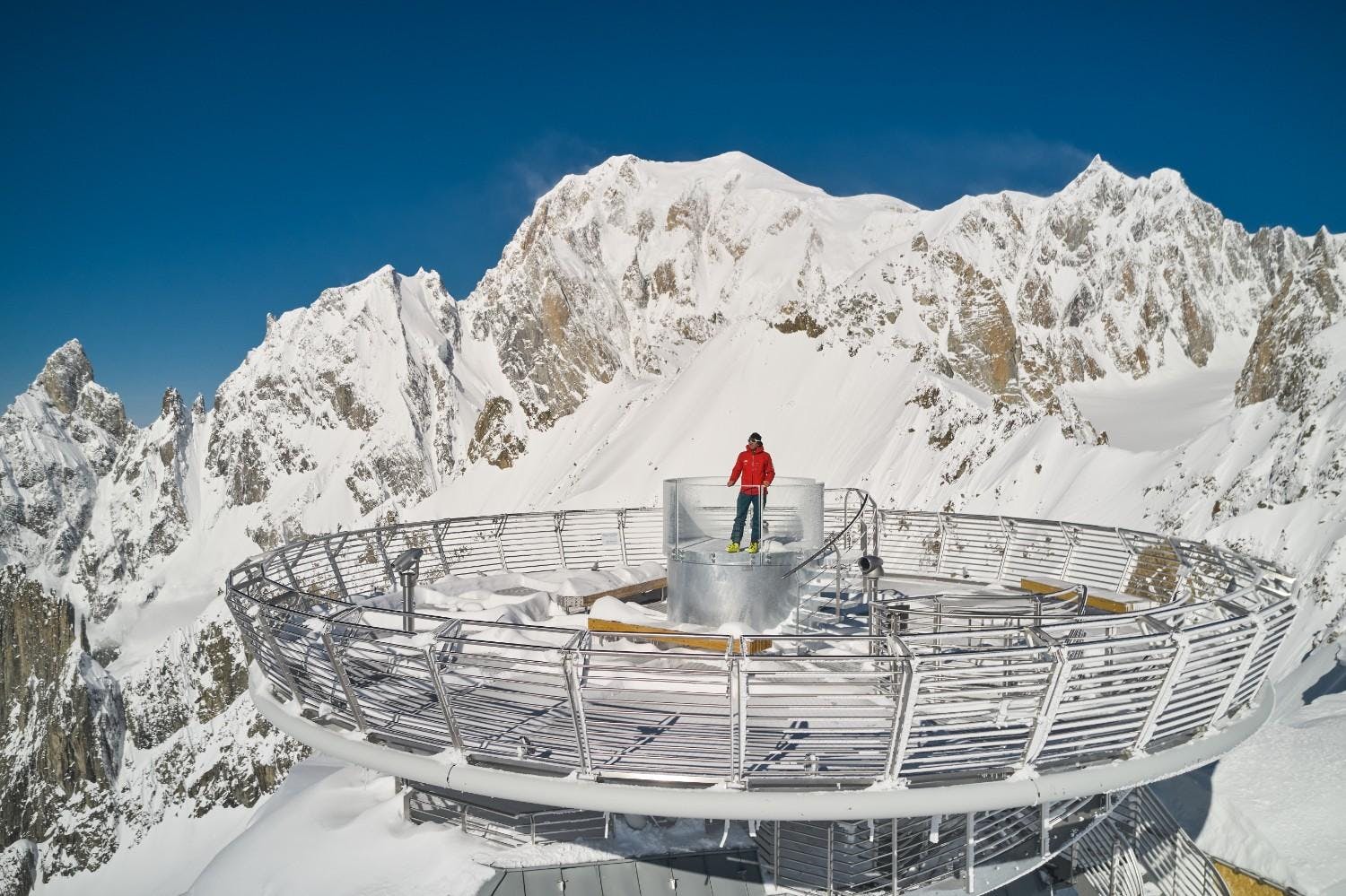 Person stands at the top of an observation deck at the top of Skyway Monte Bianco surrounded by snowy mountains