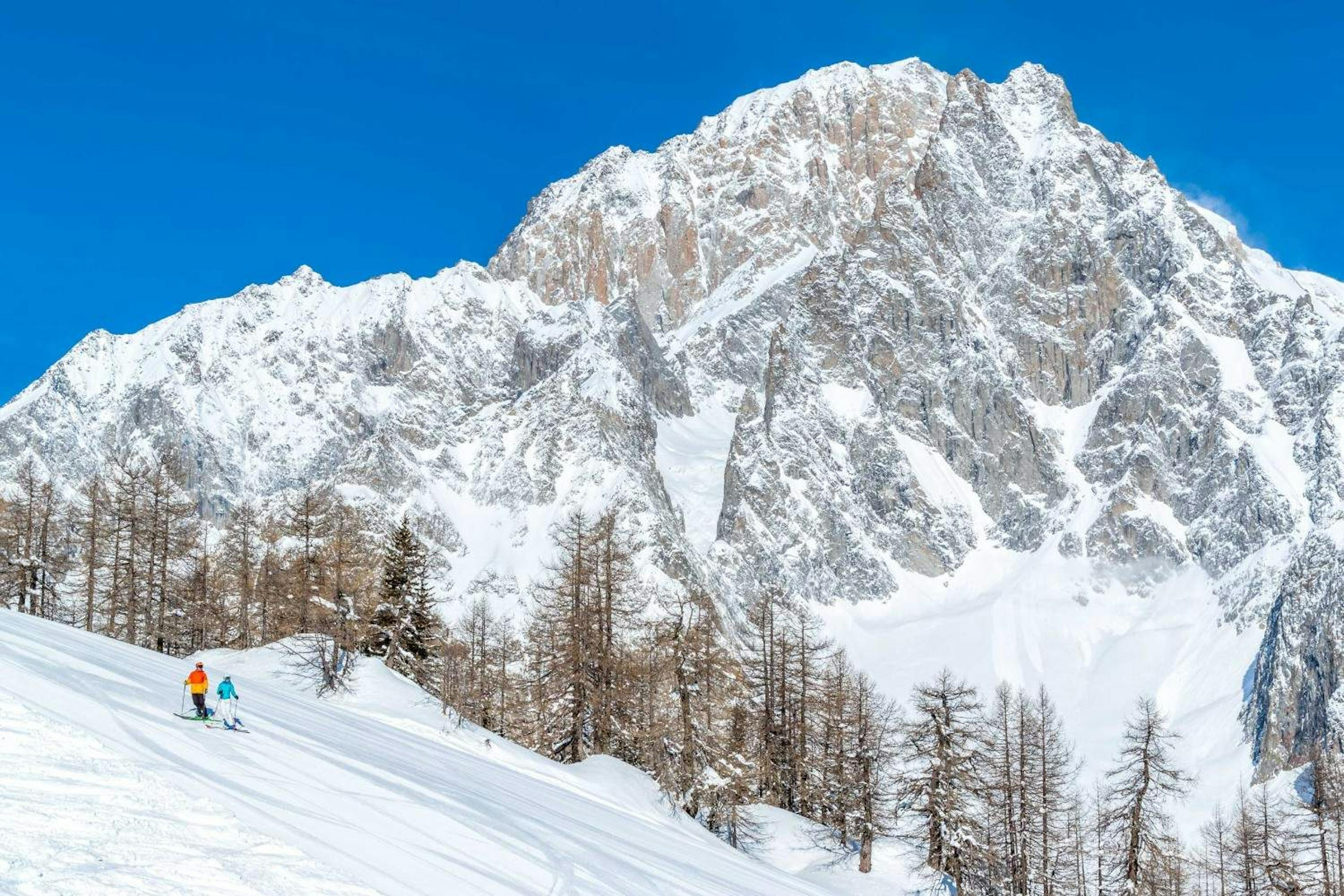 Two skiers on a run at Courmayeur Resort with snow-covered Mont Blanc behind them