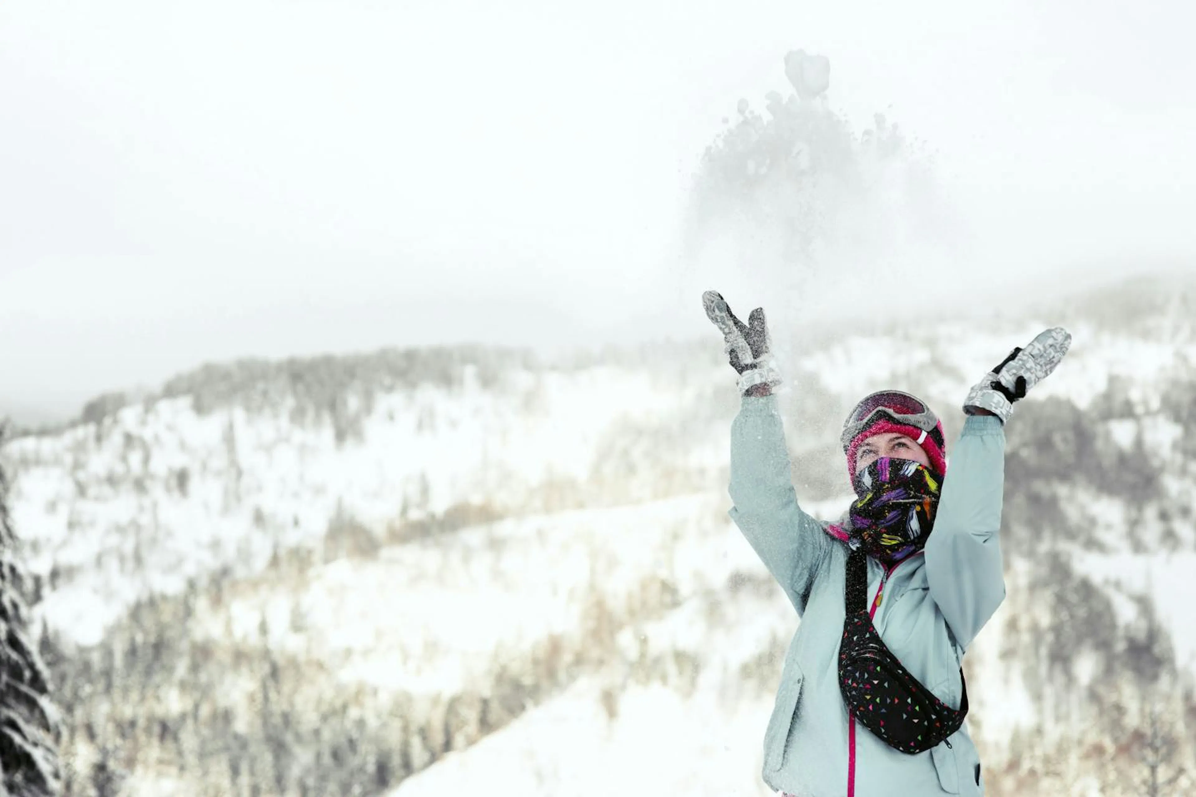 Woman watches how snow falls down on her face while she poses on the winter mountain