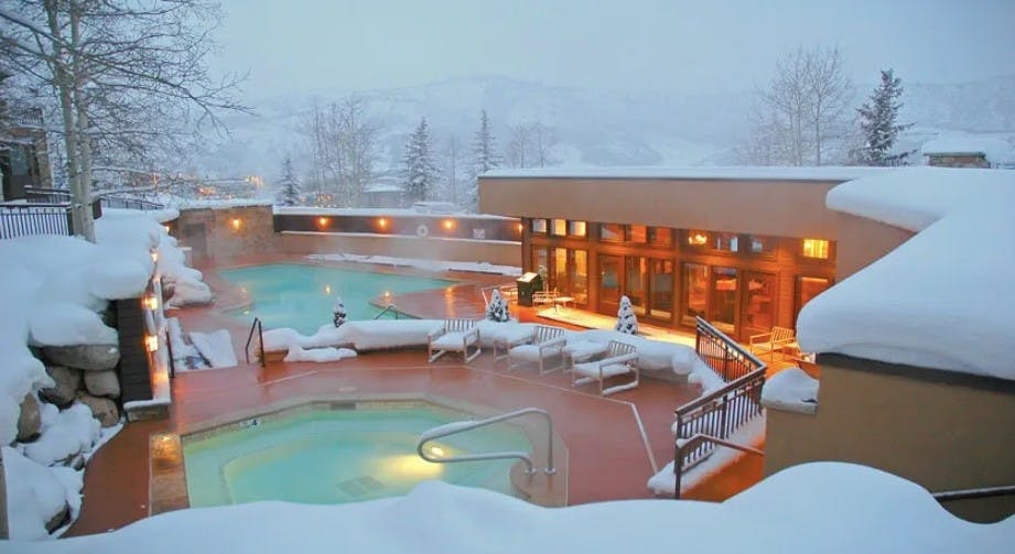 Steamy outdoor heated pool and hot tub and the snow-covered Woodrun V Lodge at Snowmass